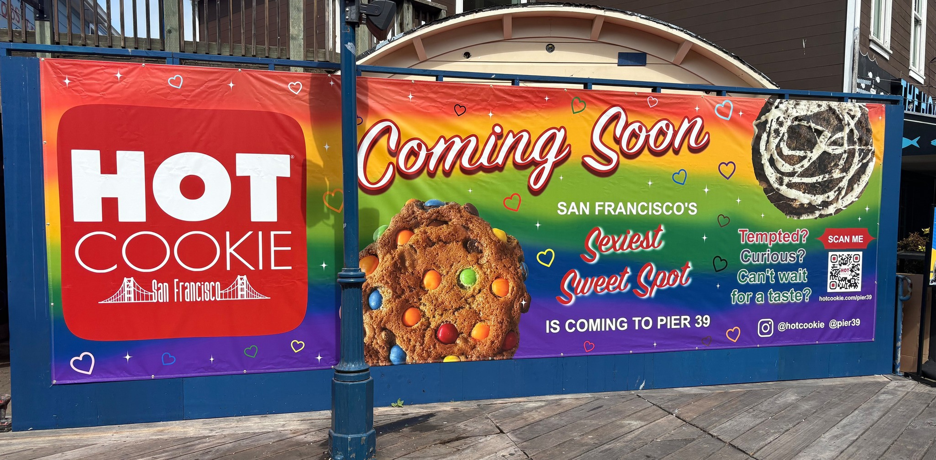 A colorful banner with rainbow background announces “Hot Cookie” coming soon to Pier 39, San Francisco, featuring images of a cookie and a cinnamon roll.