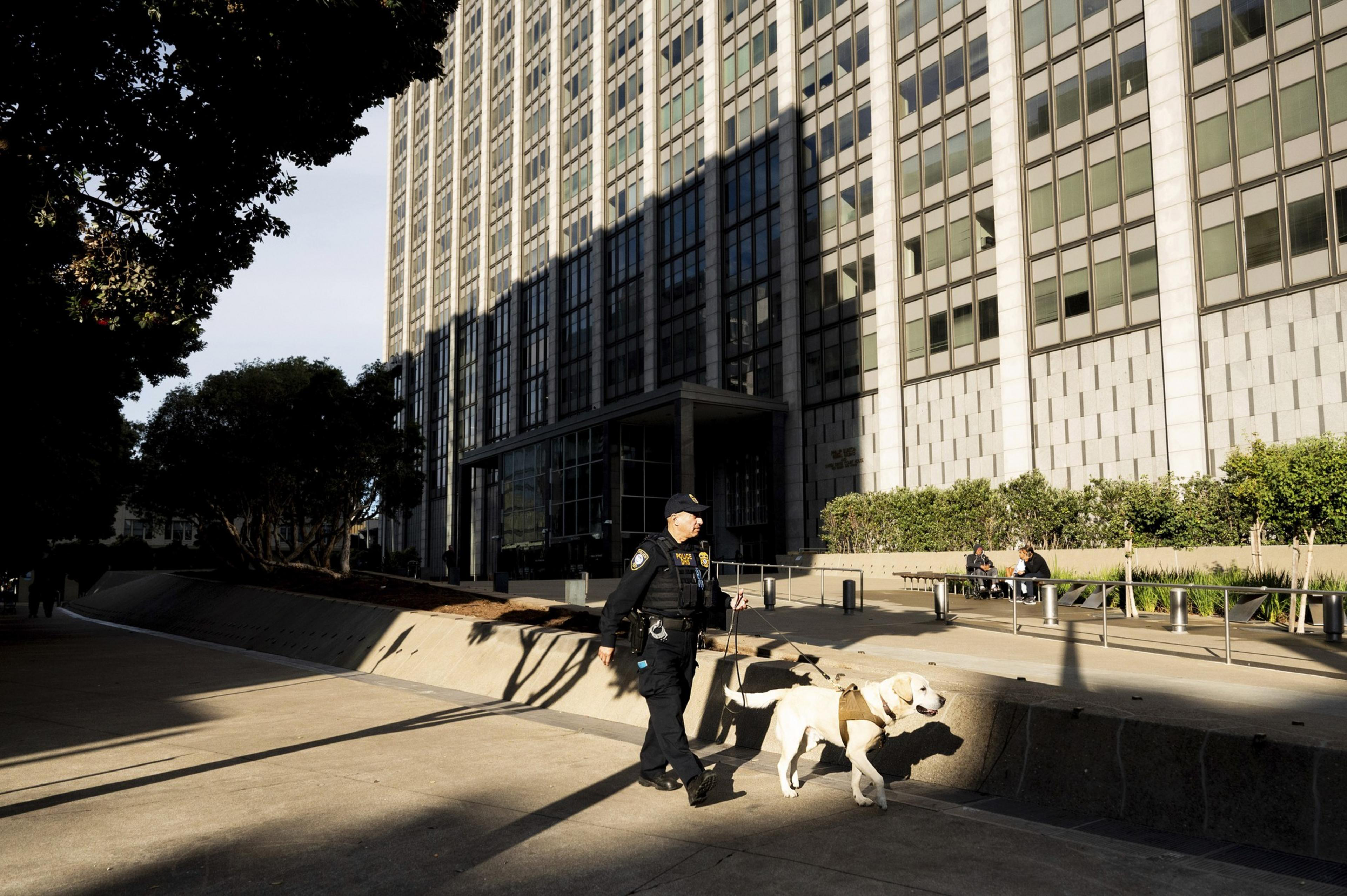 A police officer walks around the exterior a federal building with a dog.