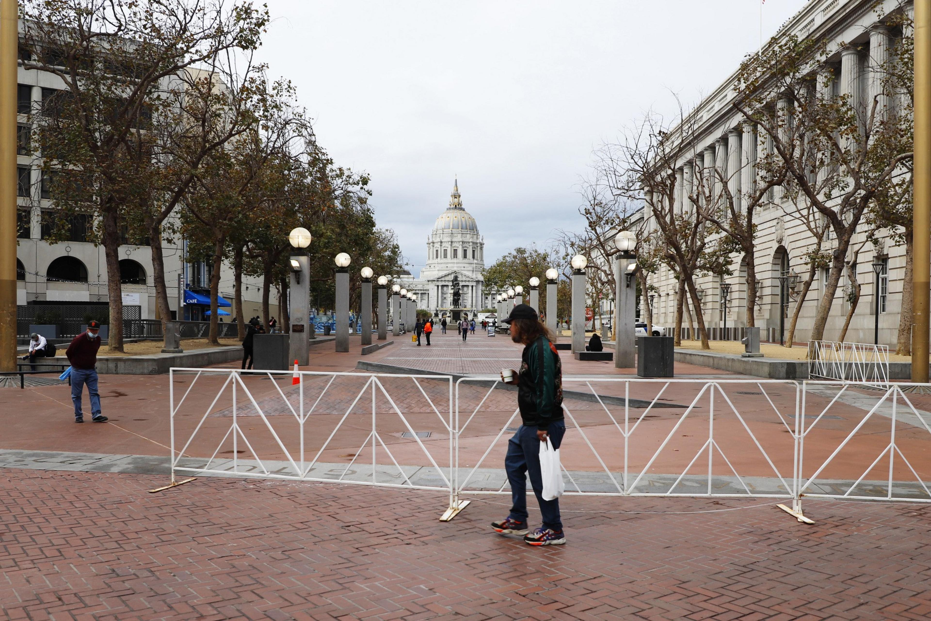 A gated plaza with a few people walking though with City Hall in the background.