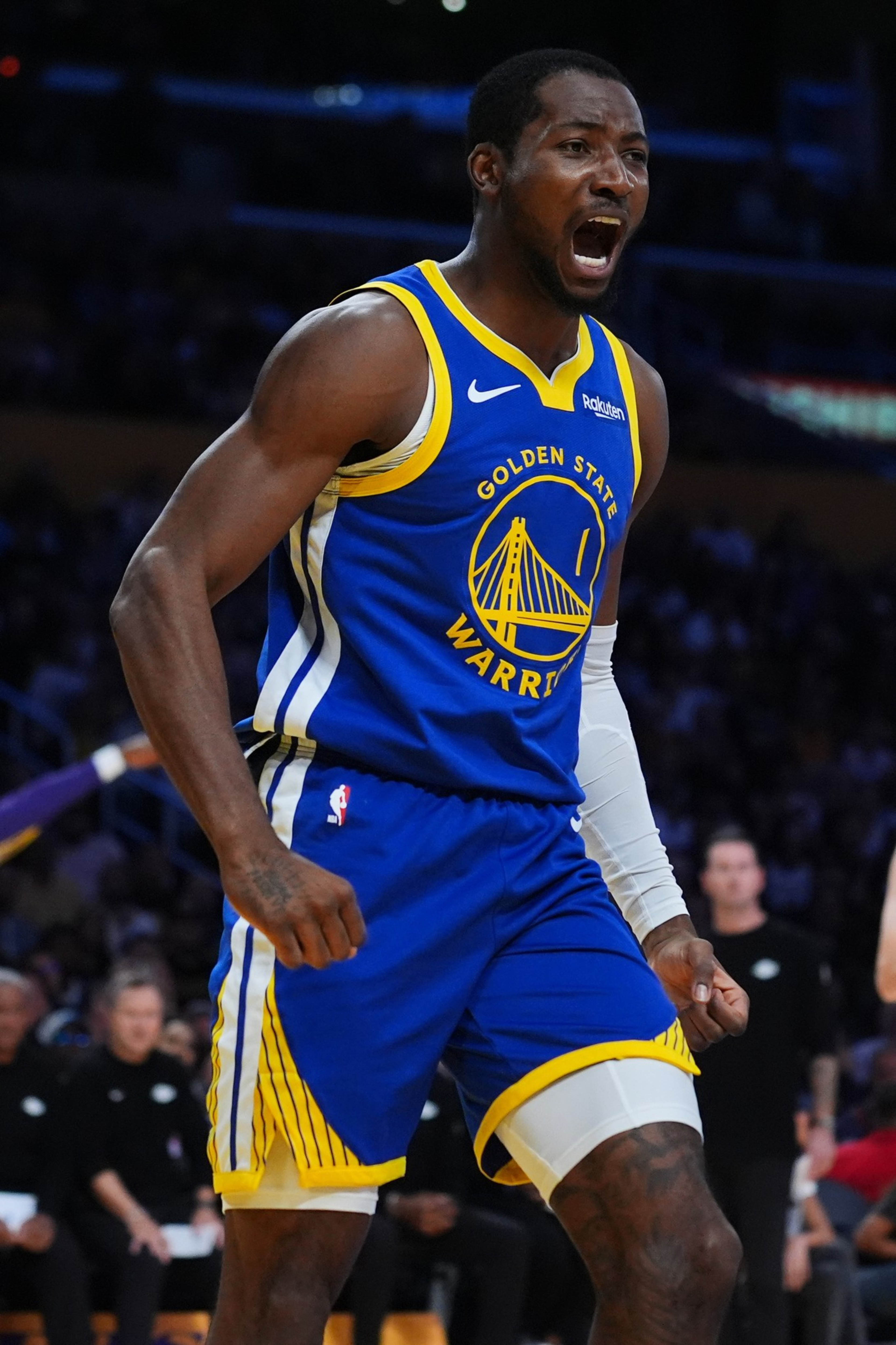 A Golden State Warriors player clenches his fists and yells passionately during an intense moment in a basketball game.