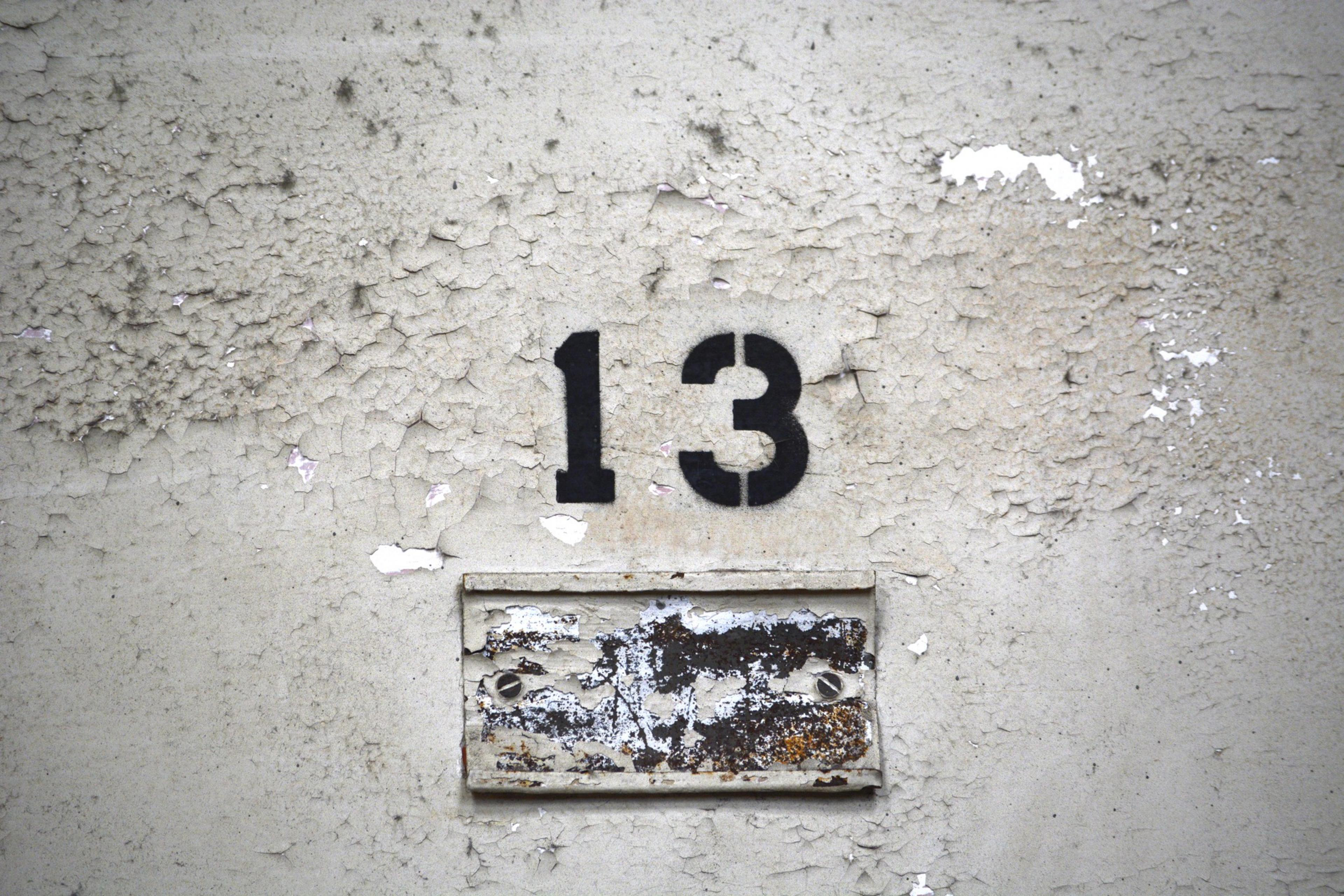 The image shows a weathered, peeling wall with the black number &quot;13&quot; stenciled above a rusted and worn metal plate.