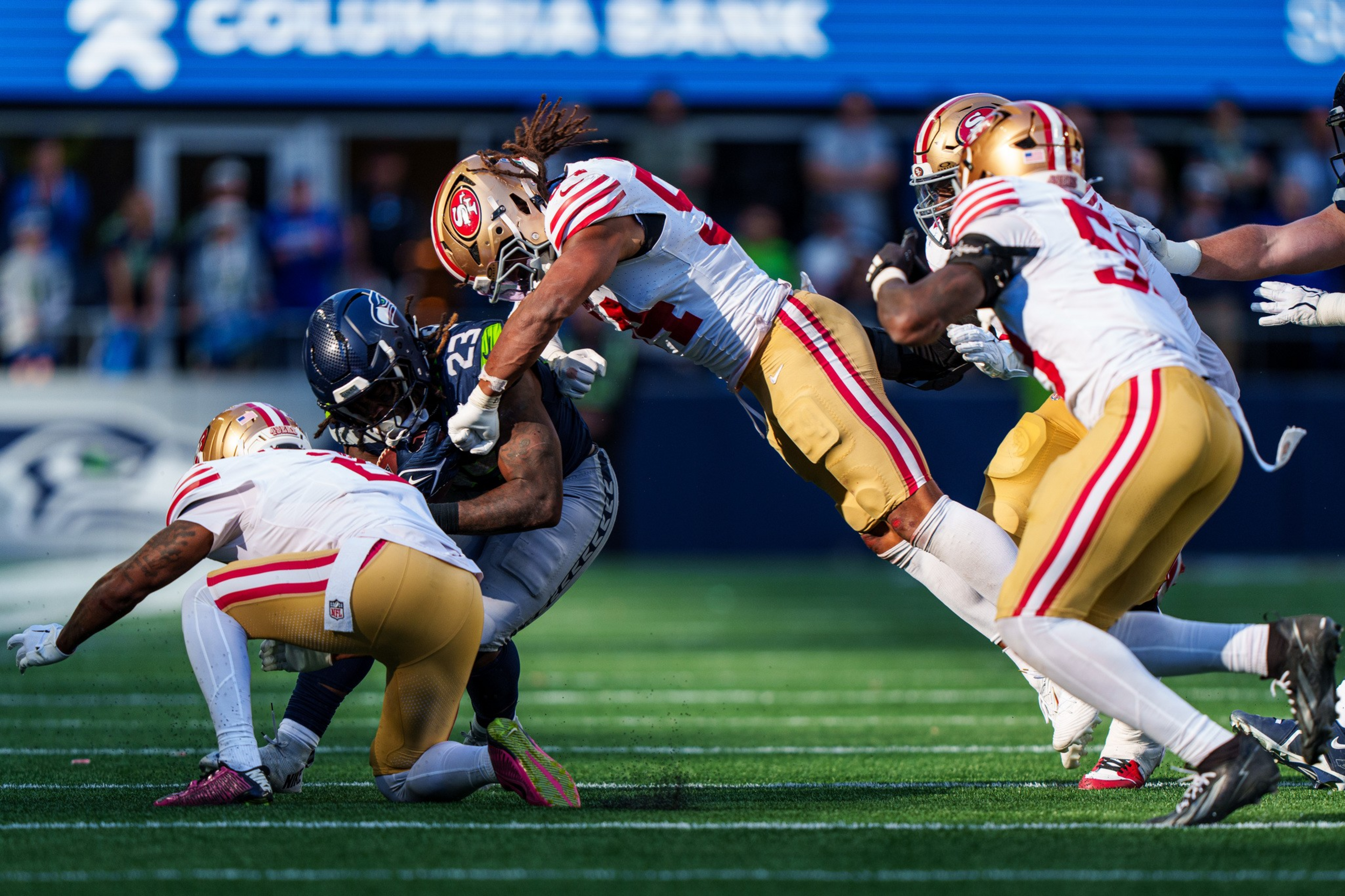 A Seattle Seahawks player is tackled by three San Francisco 49ers defenders during an intense football game on a sunlit field.