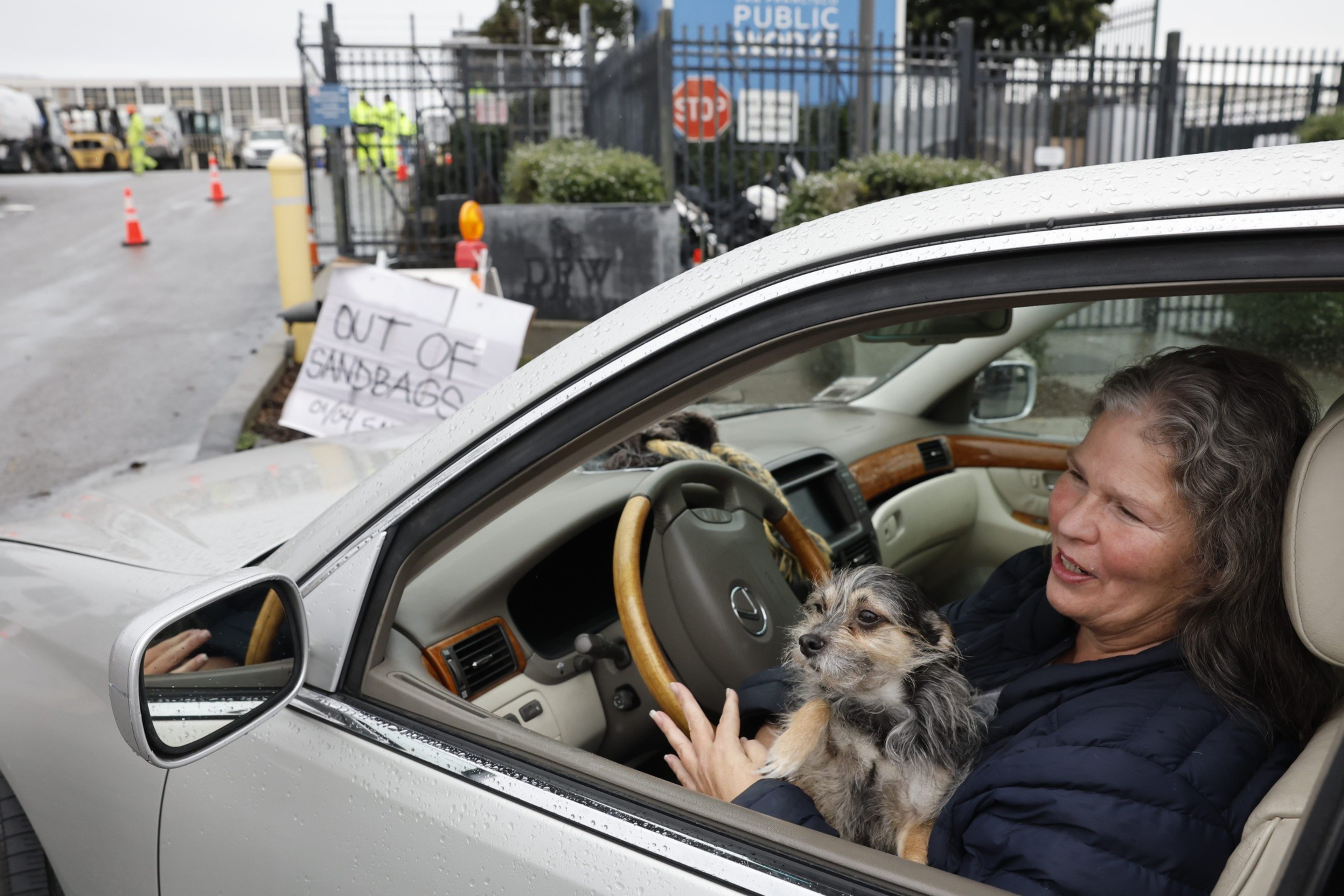 A woman carrying a small dog sits in her car awaiting sand bags during the January 2023 storms.