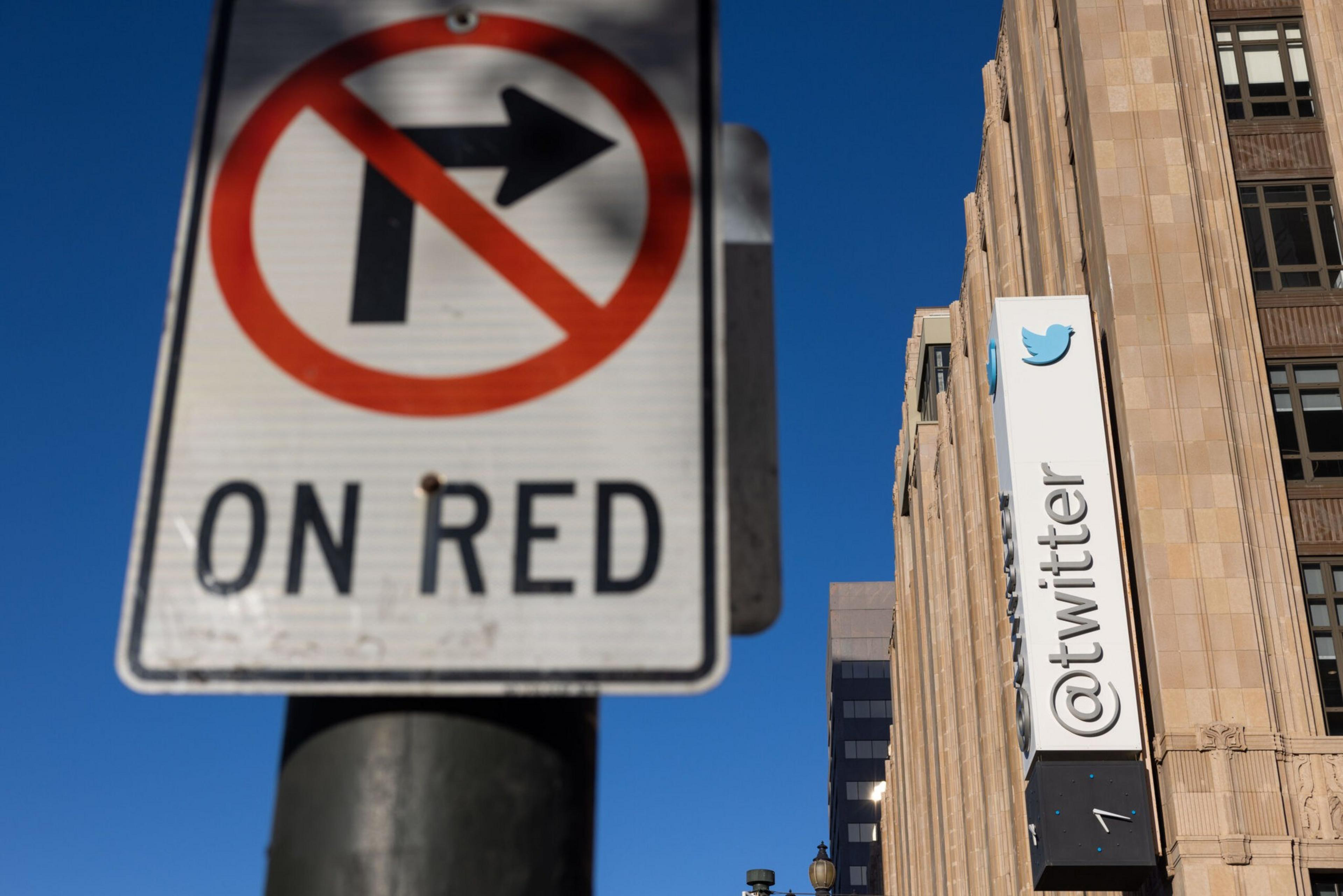 The image shows a "No Right Turn on Red" traffic sign and a building with a large "@twitter" sign on the facade, set against a clear blue sky.