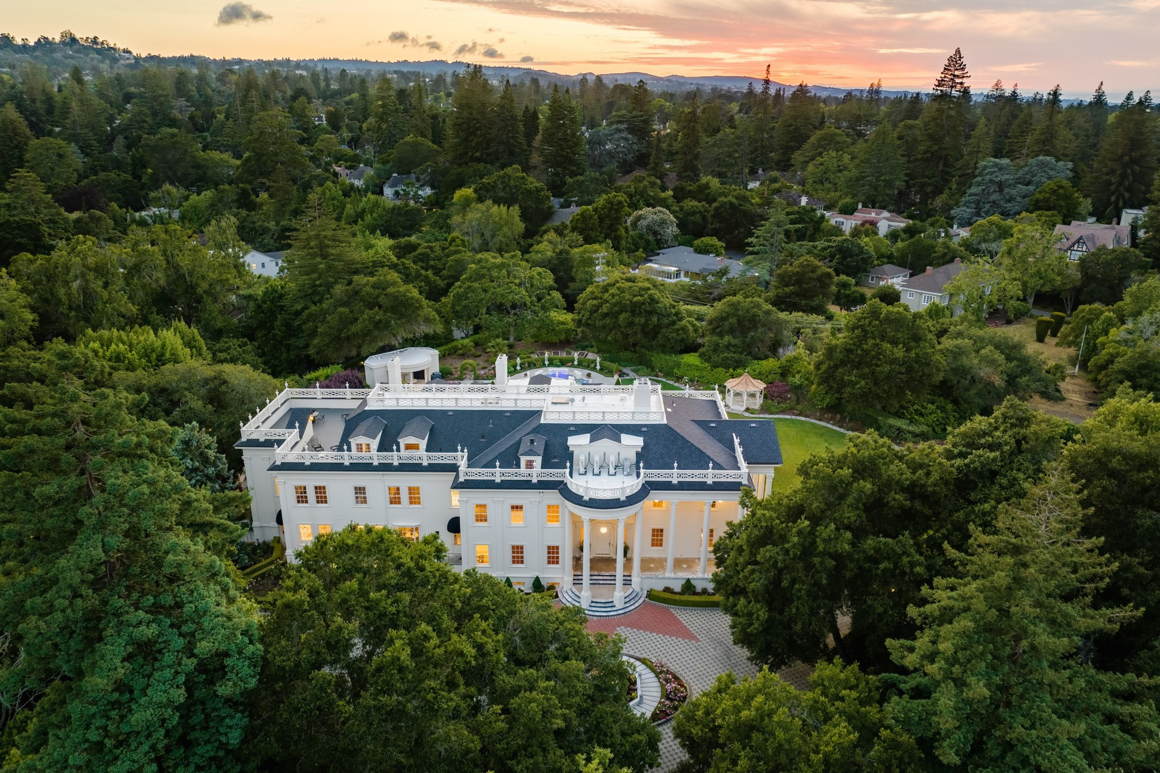 A grove of tall green trees surrounds a large white building seen from above