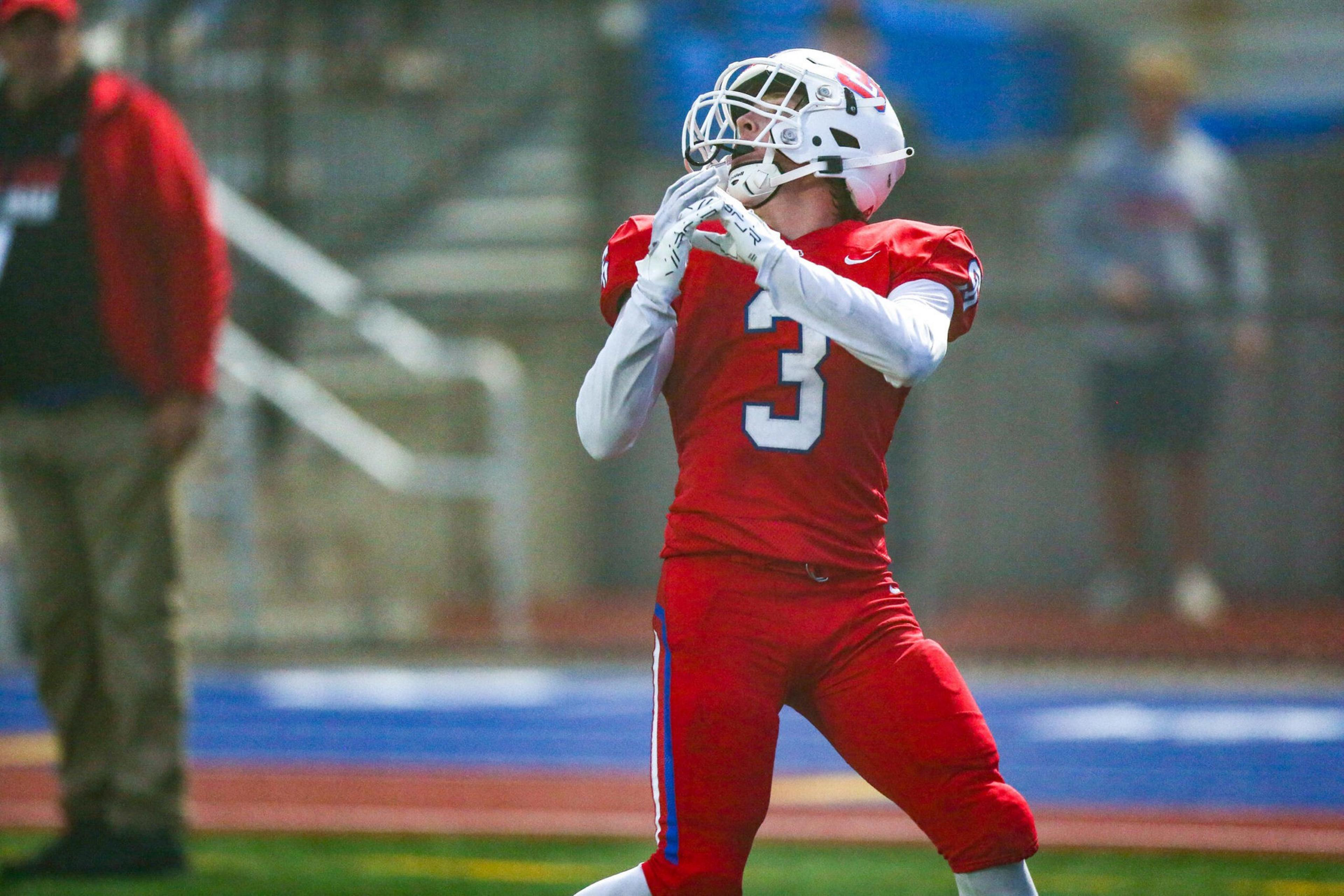 A football player wearing a red uniform and white helmet with number 3 is preparing to catch a football during a game.
