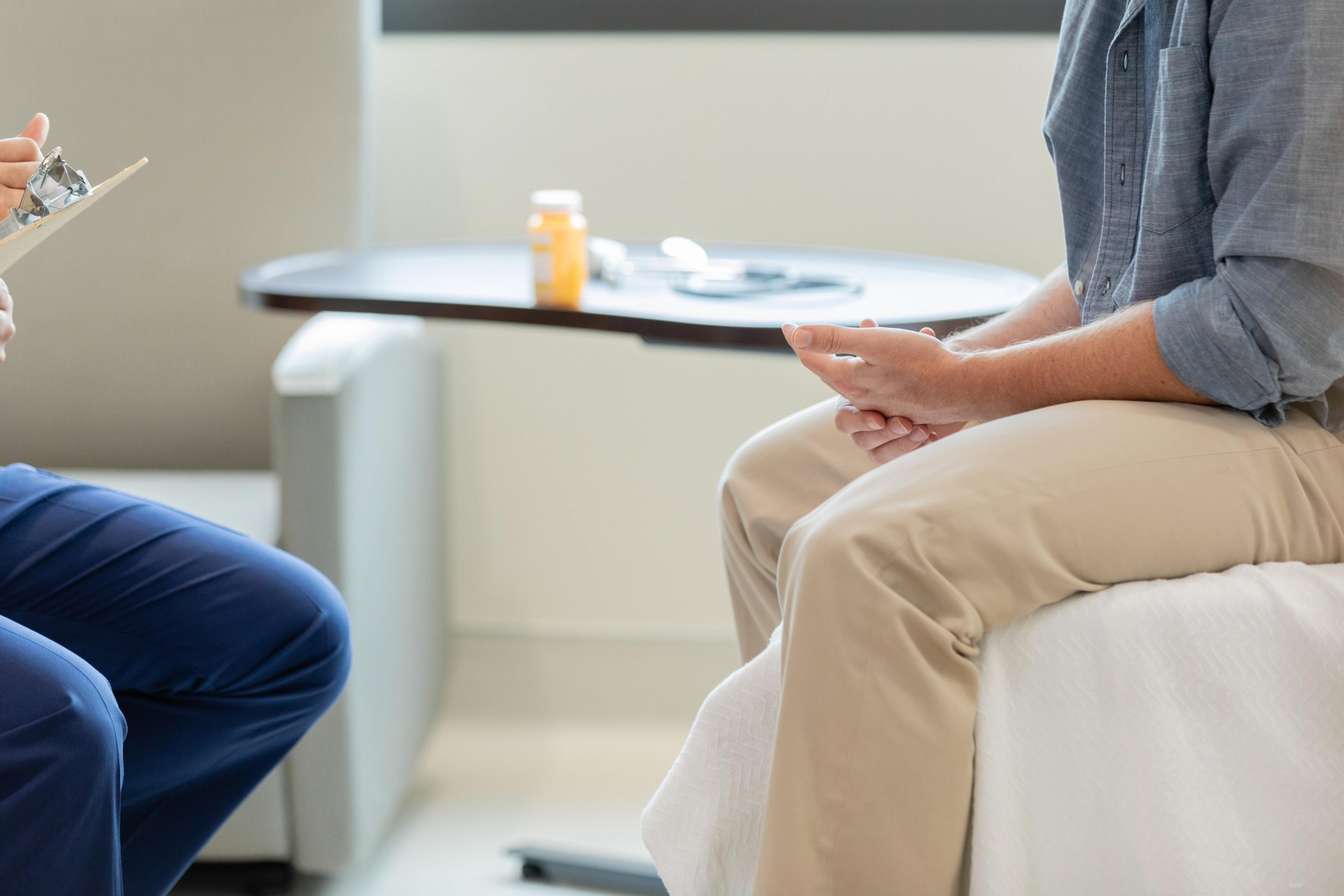 a person sits across from another person in a fgrey shirt and tan pants.