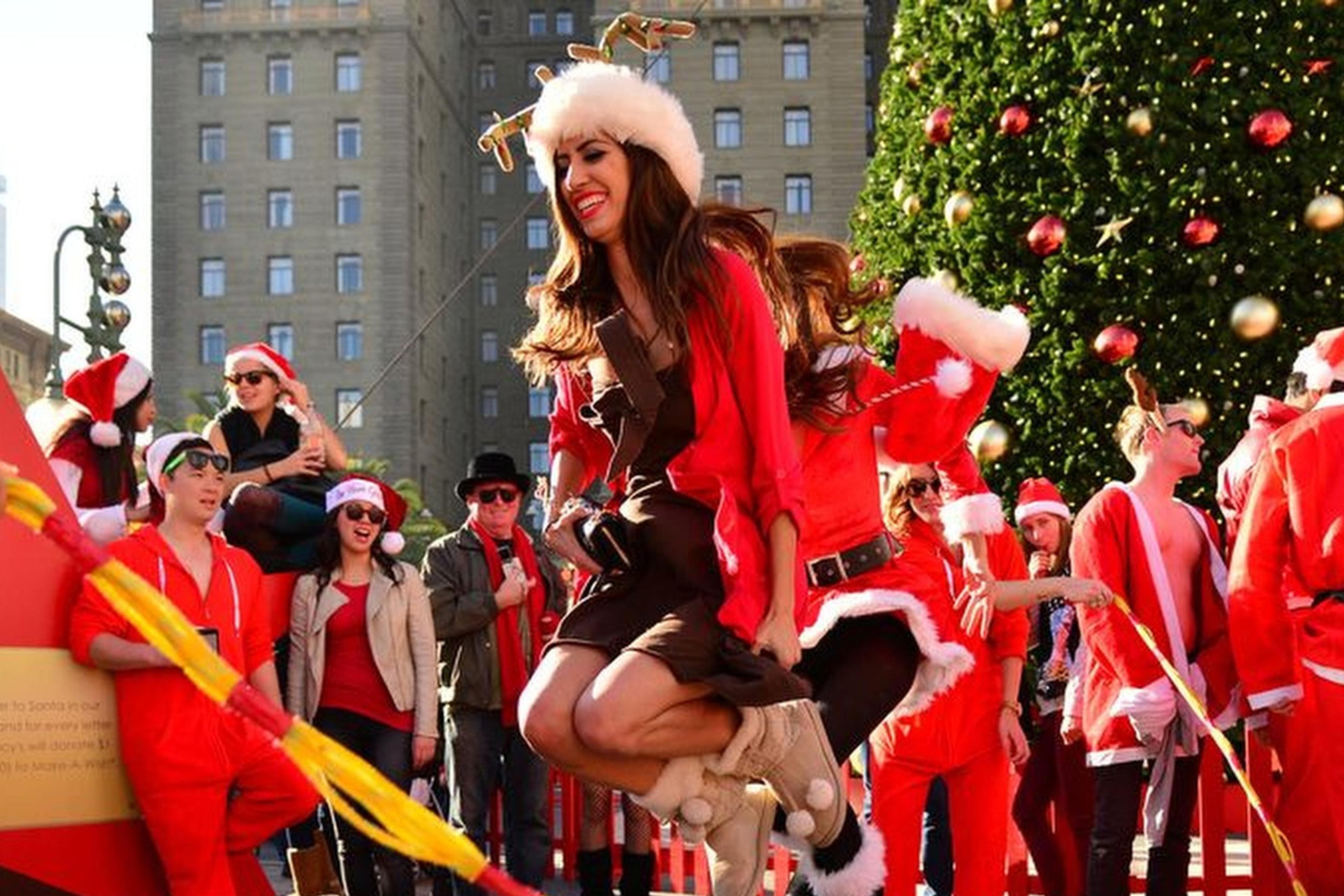 Several people in red Santa Clause outfits stand around a tree.