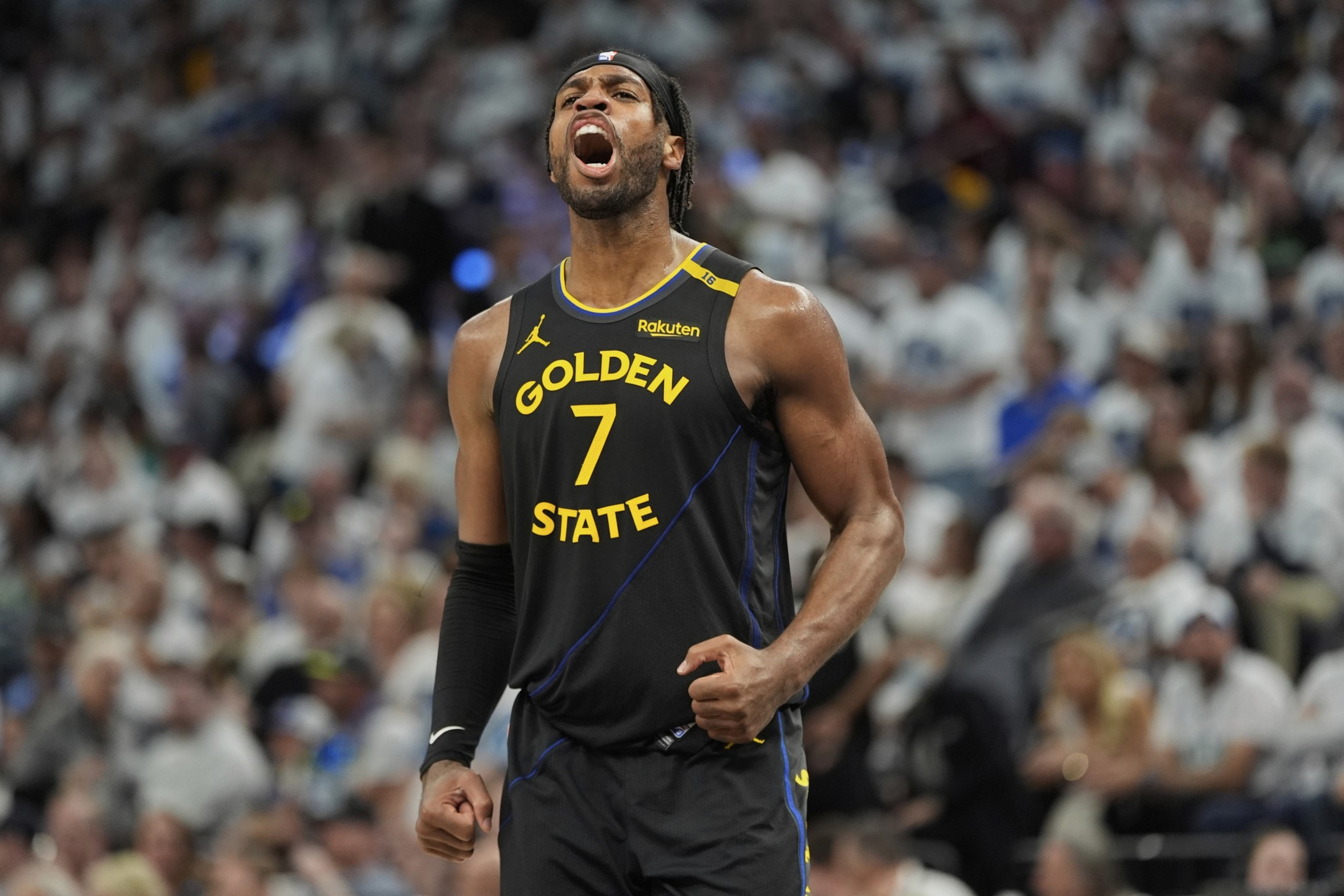 A basketball player in a black &quot;Golden State&quot; jersey, number 7, is passionately shouting on the court, with a crowd blurred in the background.
