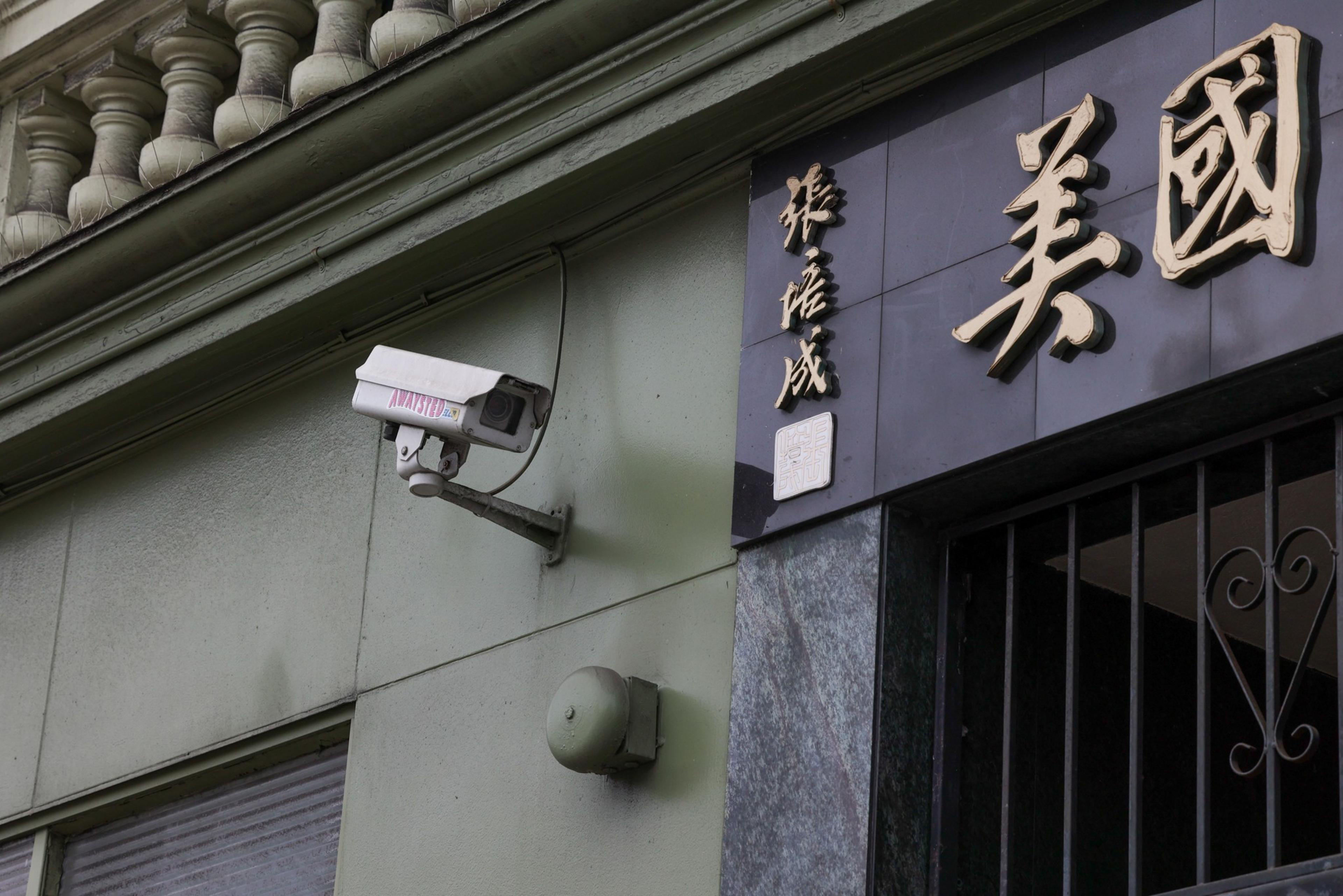 A weathered security camera mounted on a wall next to Asian characters and an emblem.