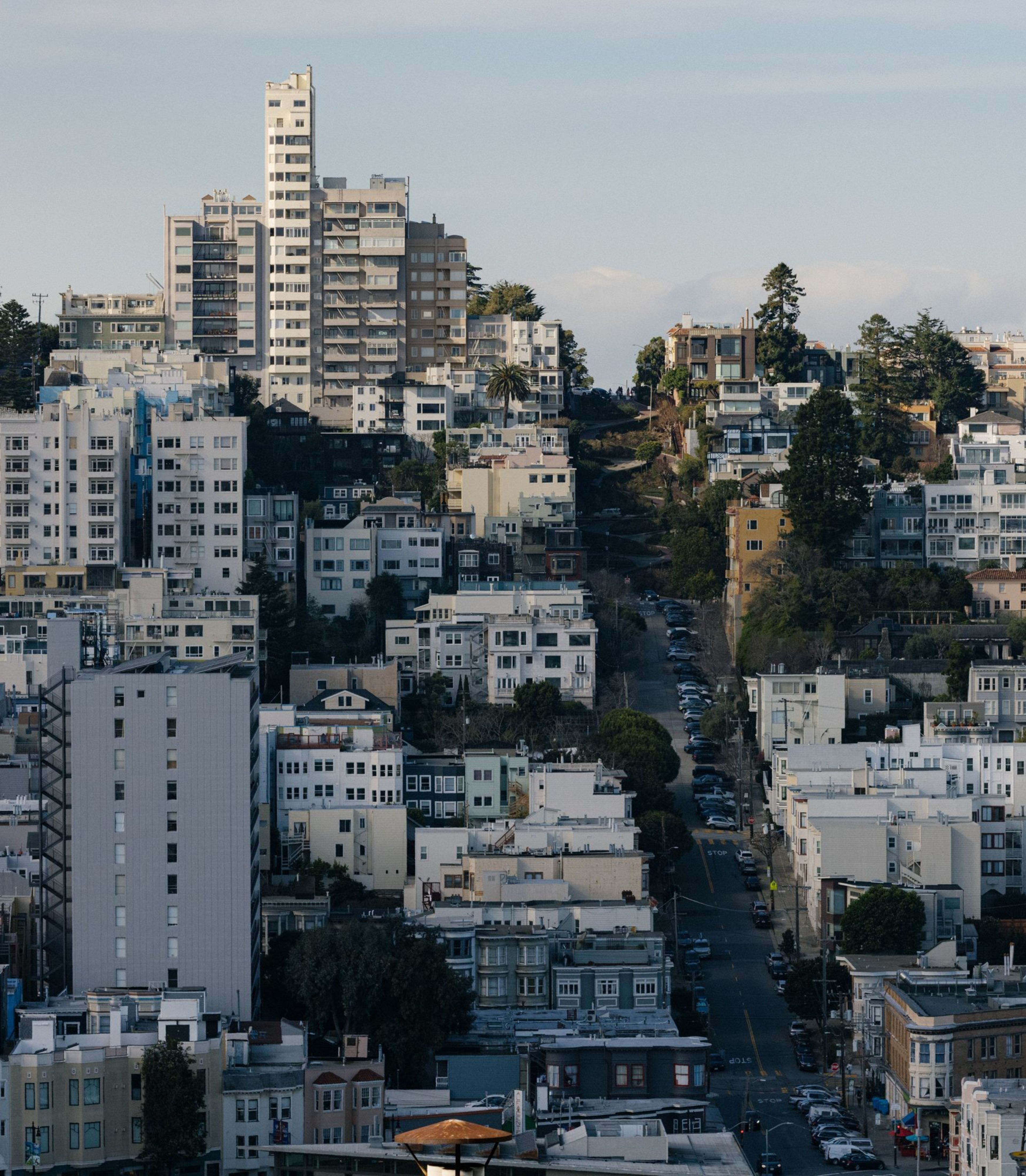 Dense urban area with multi-story buildings on a sloping hill, under a clear sky.