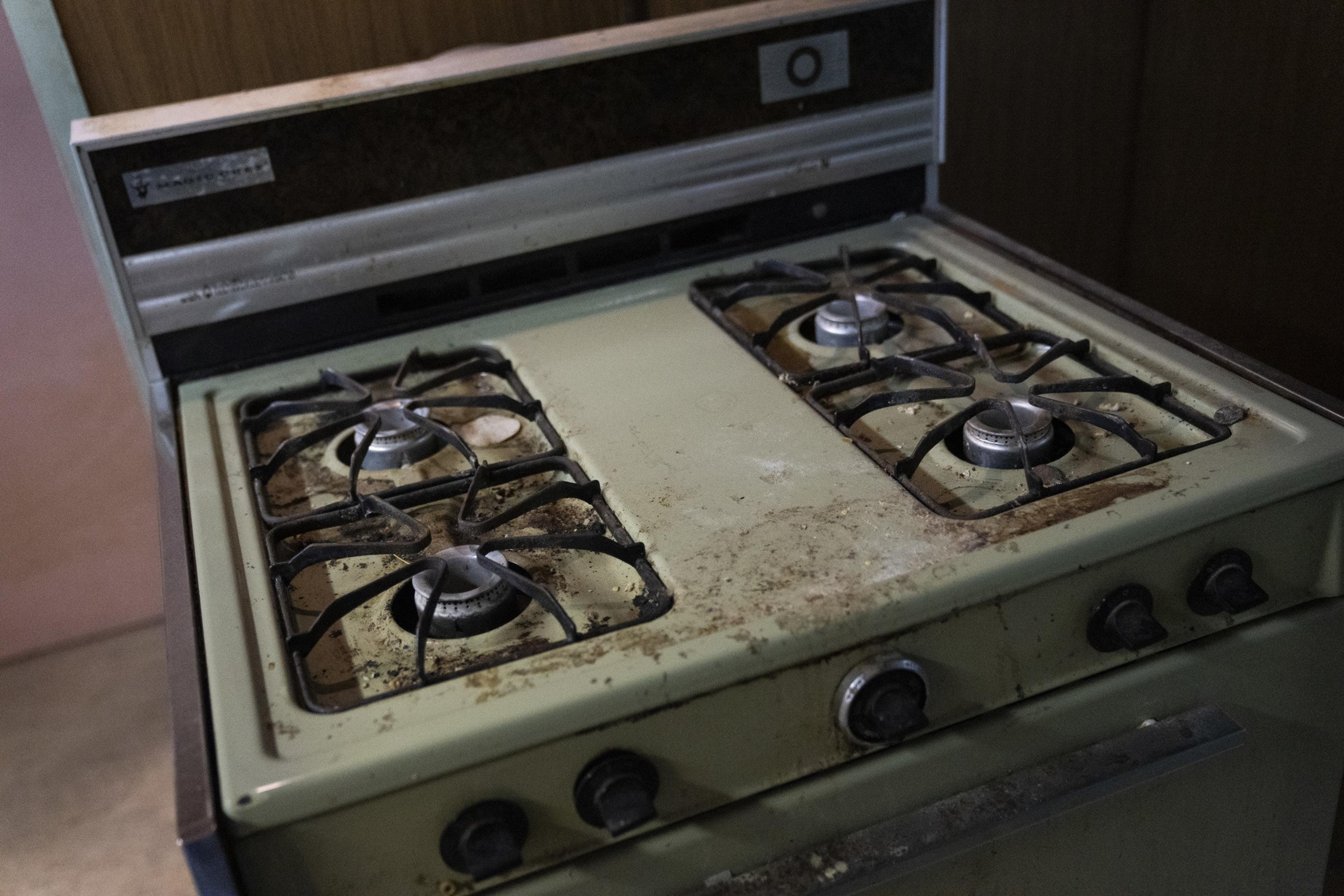 The image shows an old, dirty gas stove with four burners and grime accumulated on the green metal surface and surrounding knobs.