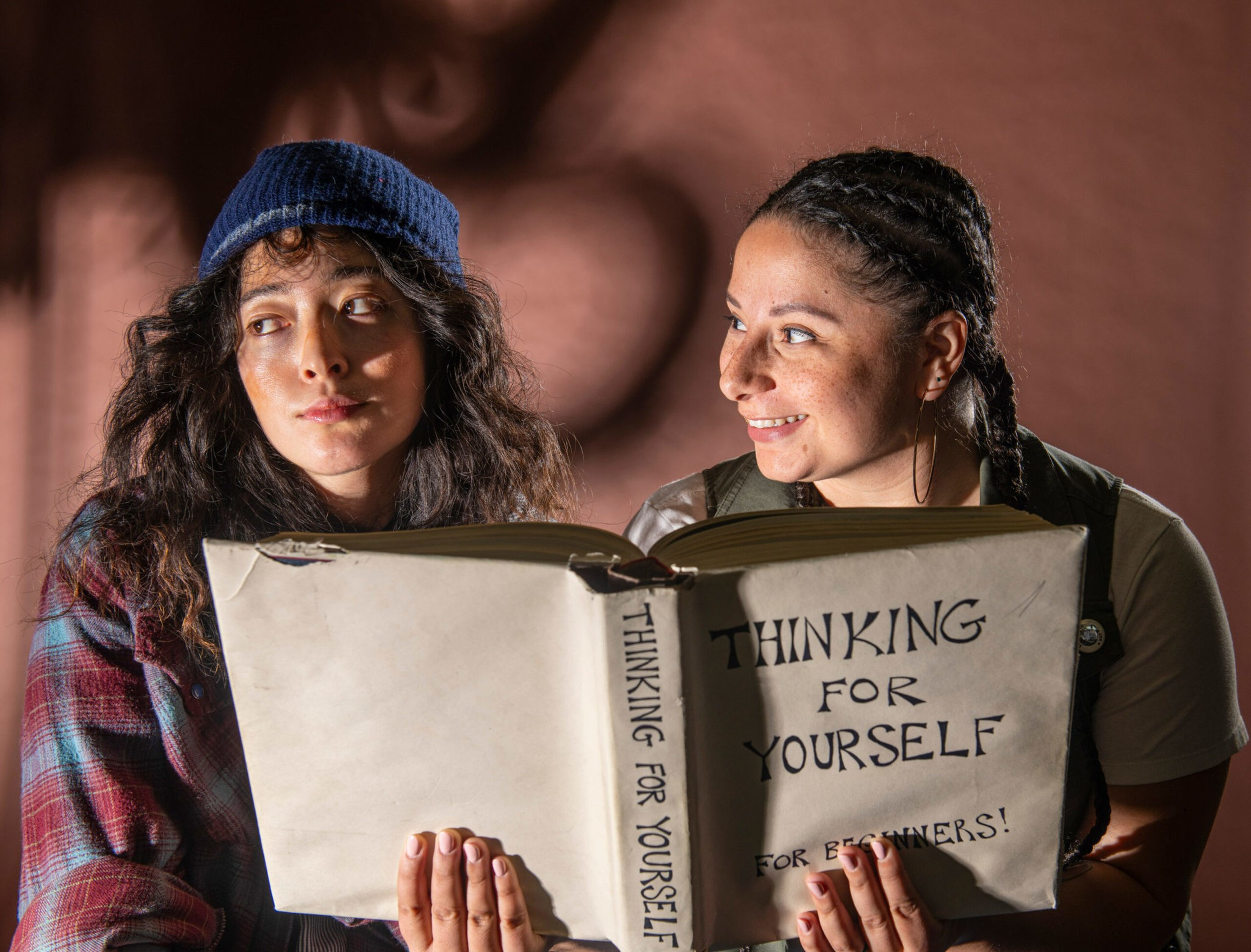 Two people hold an open book titled "Thinking for Yourself for Beginners!" One looks serious, the other smiles warmly.