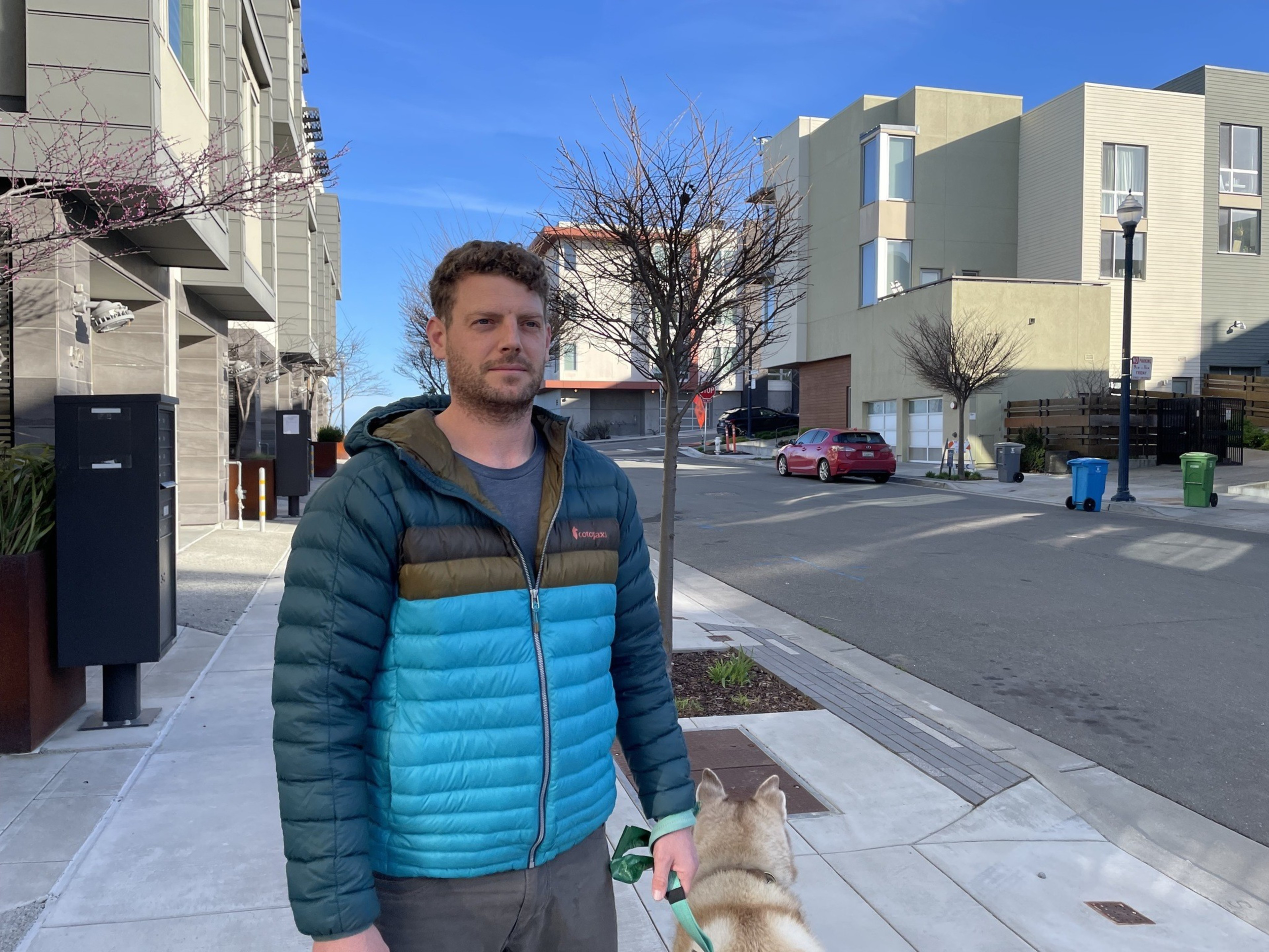 A man stands on the sidewalk holding a dog on a leash.
