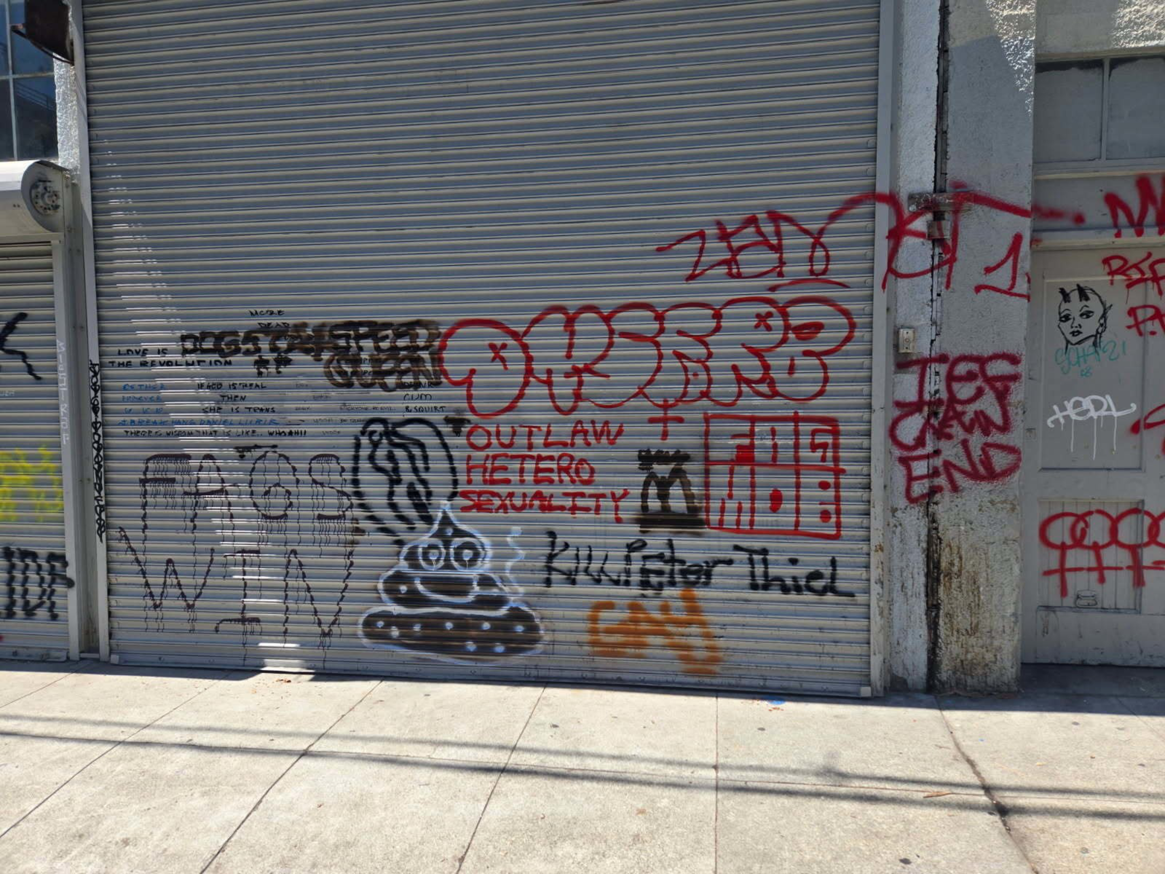 A gray metal garage door is covered with various graffiti, including stylized text, symbols, and drawings in red, black, and several other colors.