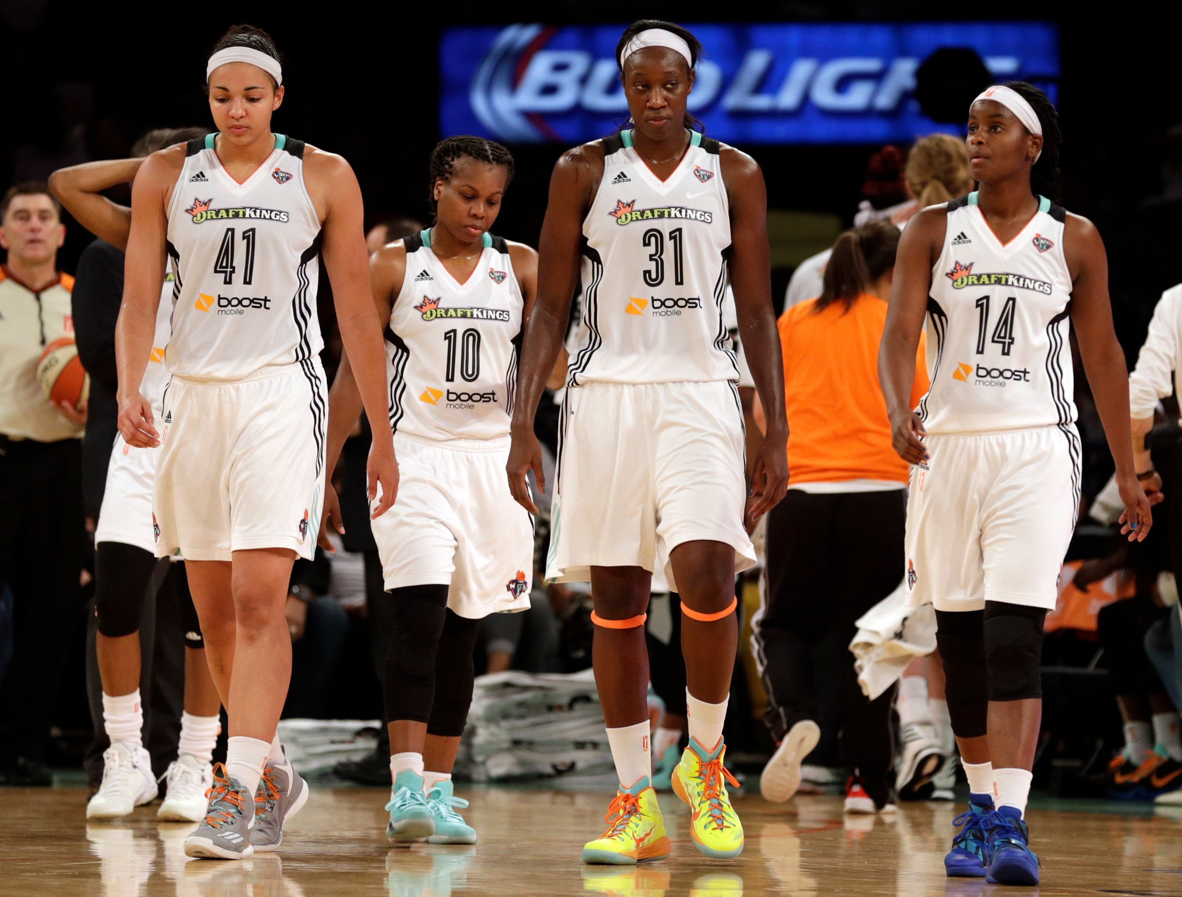 Four female basketball players in white jerseys with DraftKings and Boost Mobile logos walk on the court, looking focused and serious.