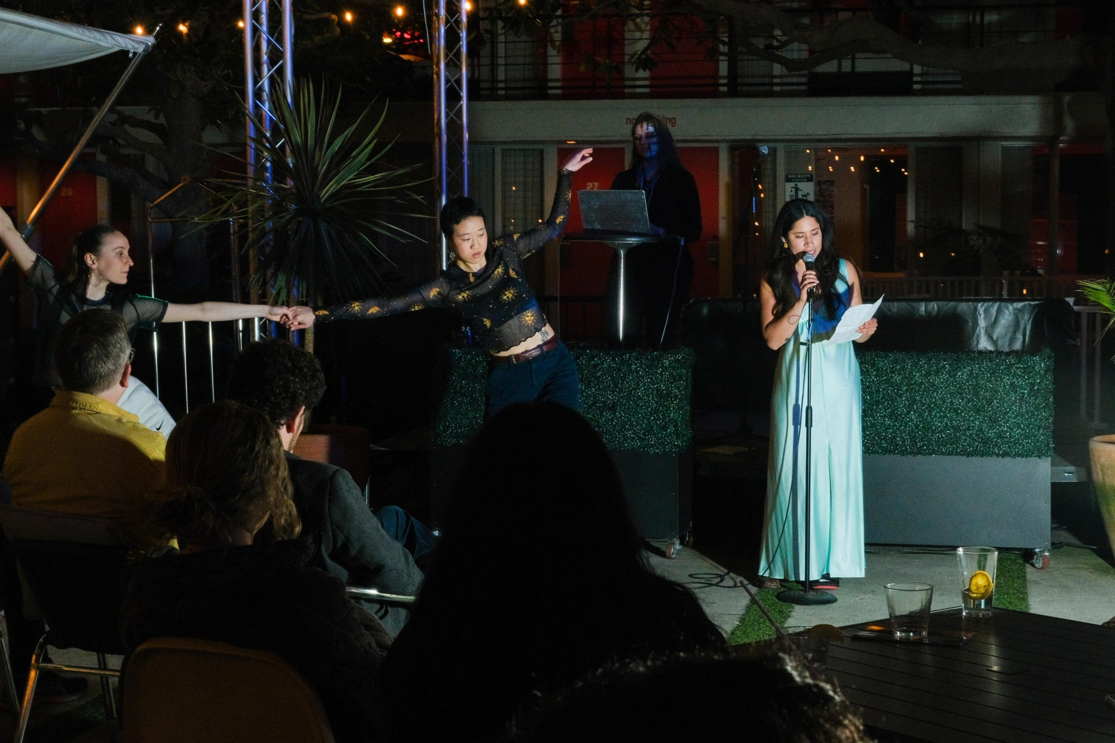 Two dancers perform beside a speaker at an outdoor evening event.