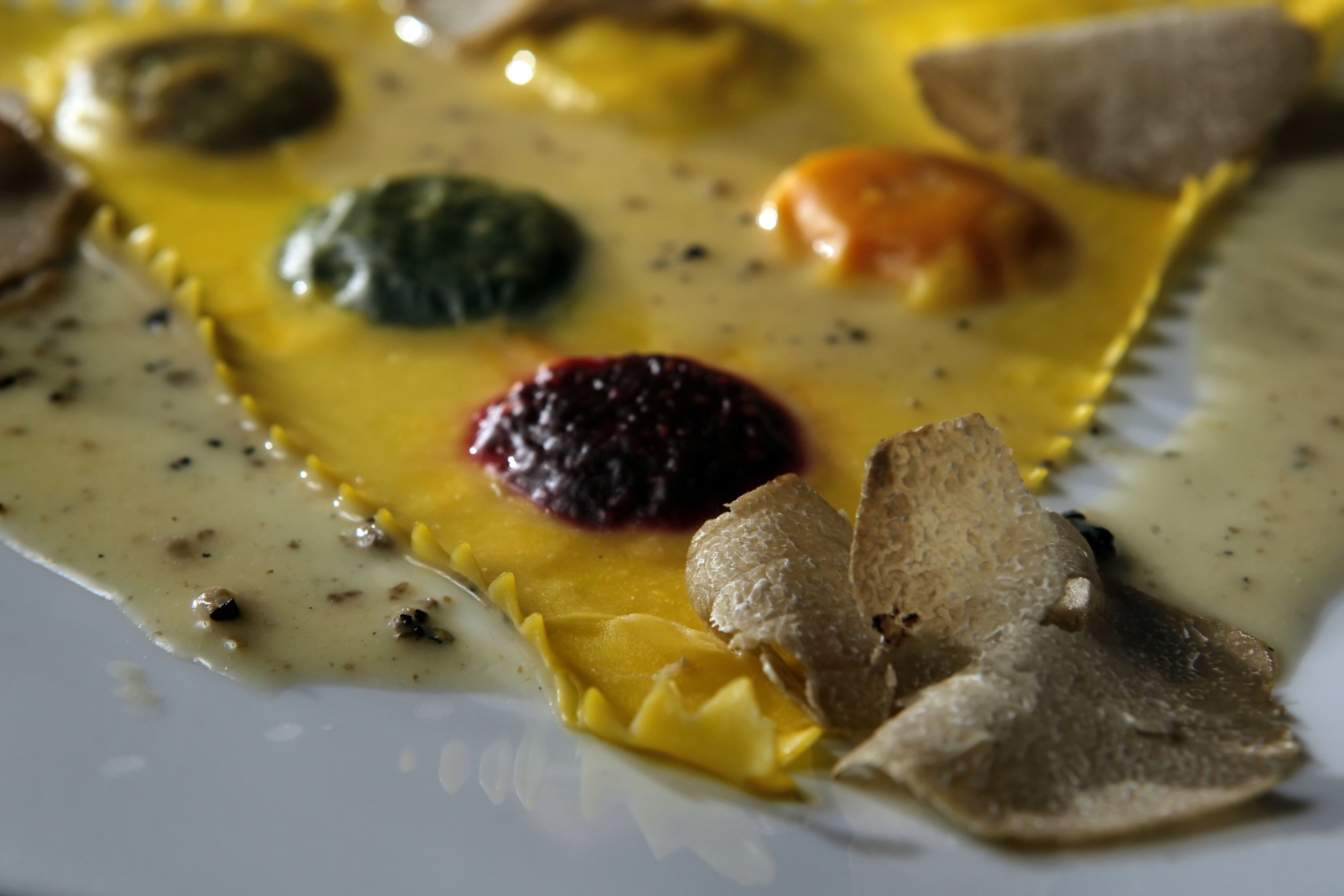 A close-up of ravioli is shown with various sauces and black truffles.