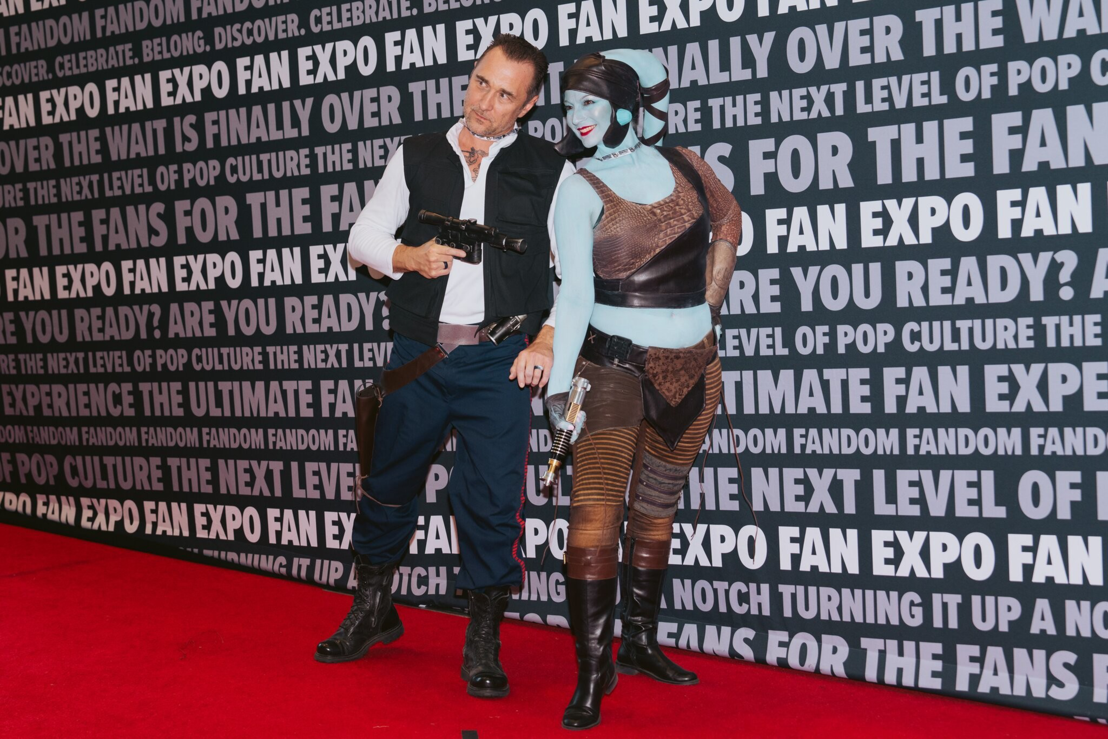 A costumed man and woman stand in front of a step-and-repeat.