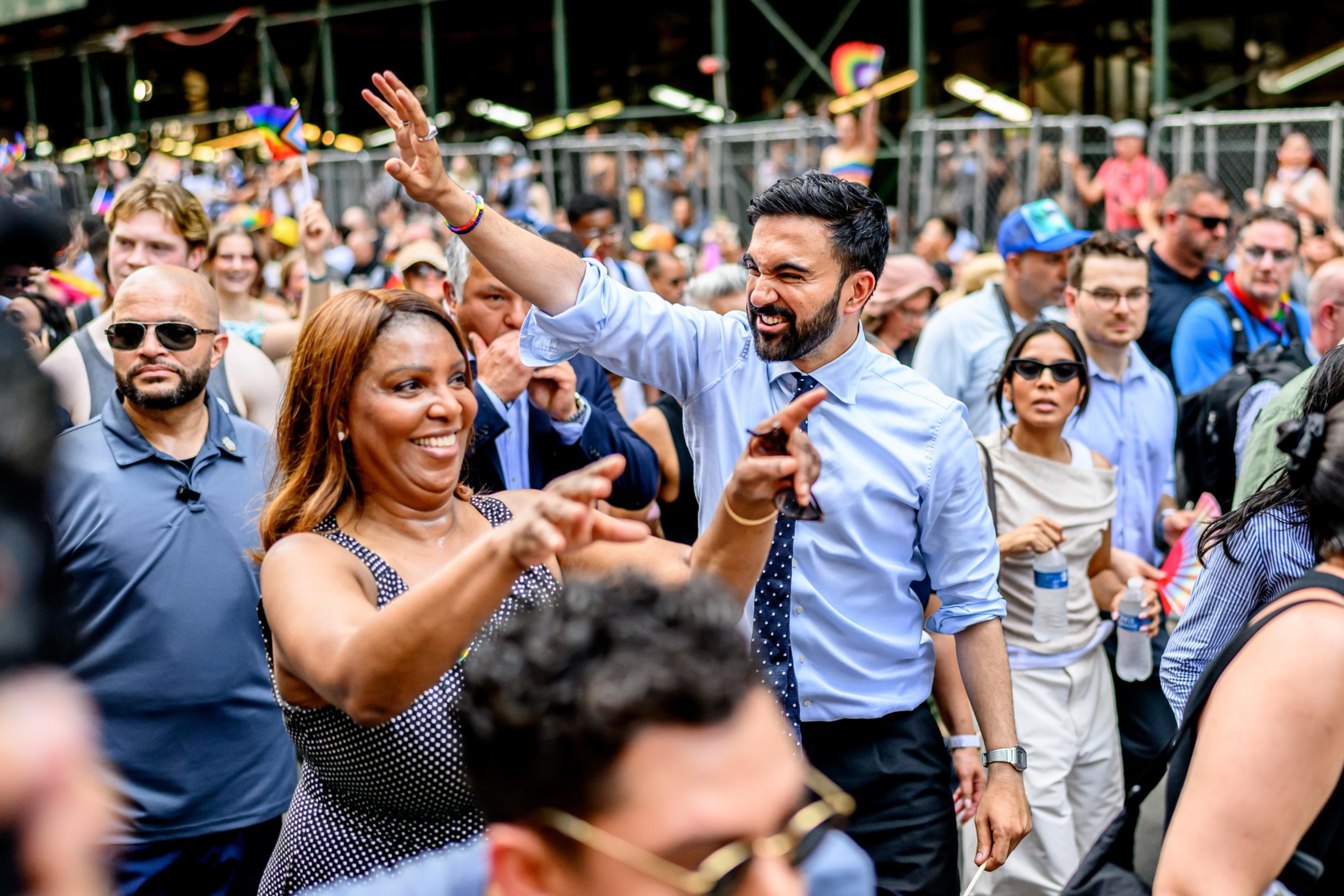 A diverse crowd dances and smiles energetically, with a man in a blue shirt and tie and a woman in a polka-dot dress leading the joyful motion.