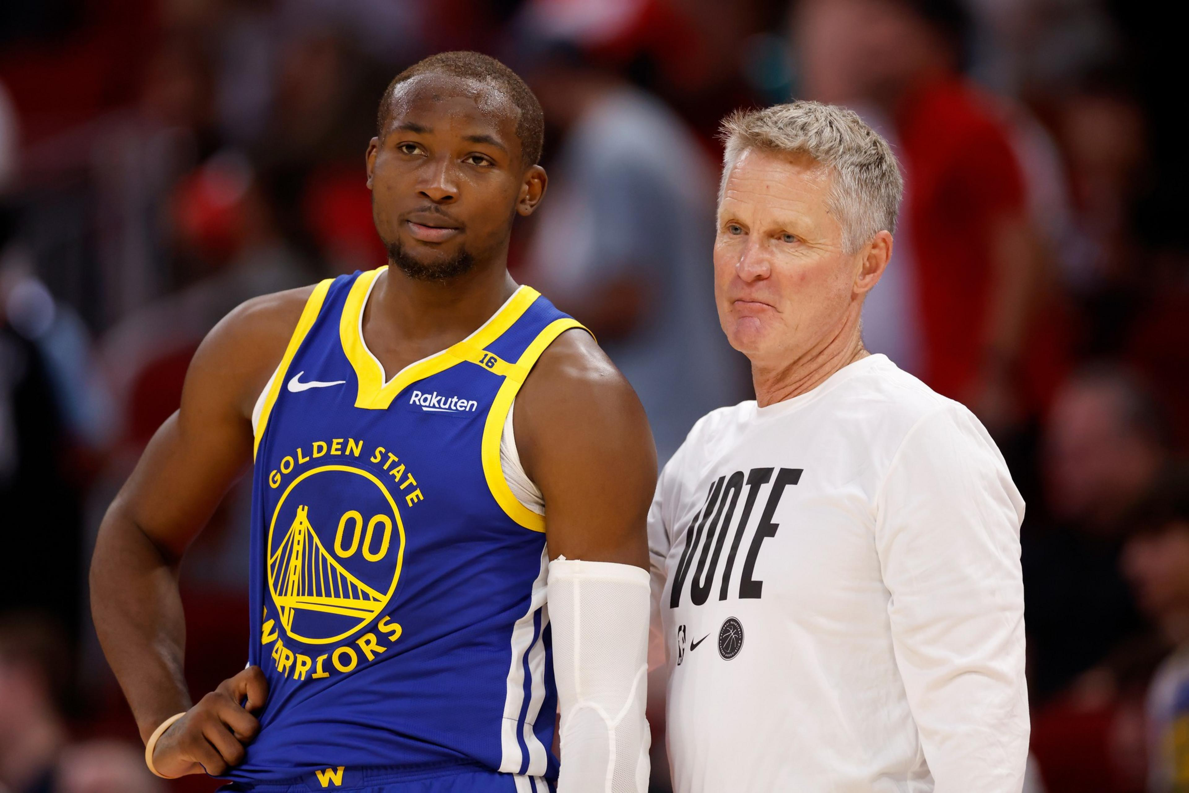 A basketball player in a blue Golden State Warriors jersey stands beside a person in a white shirt with &quot;VOTE&quot; written on it.