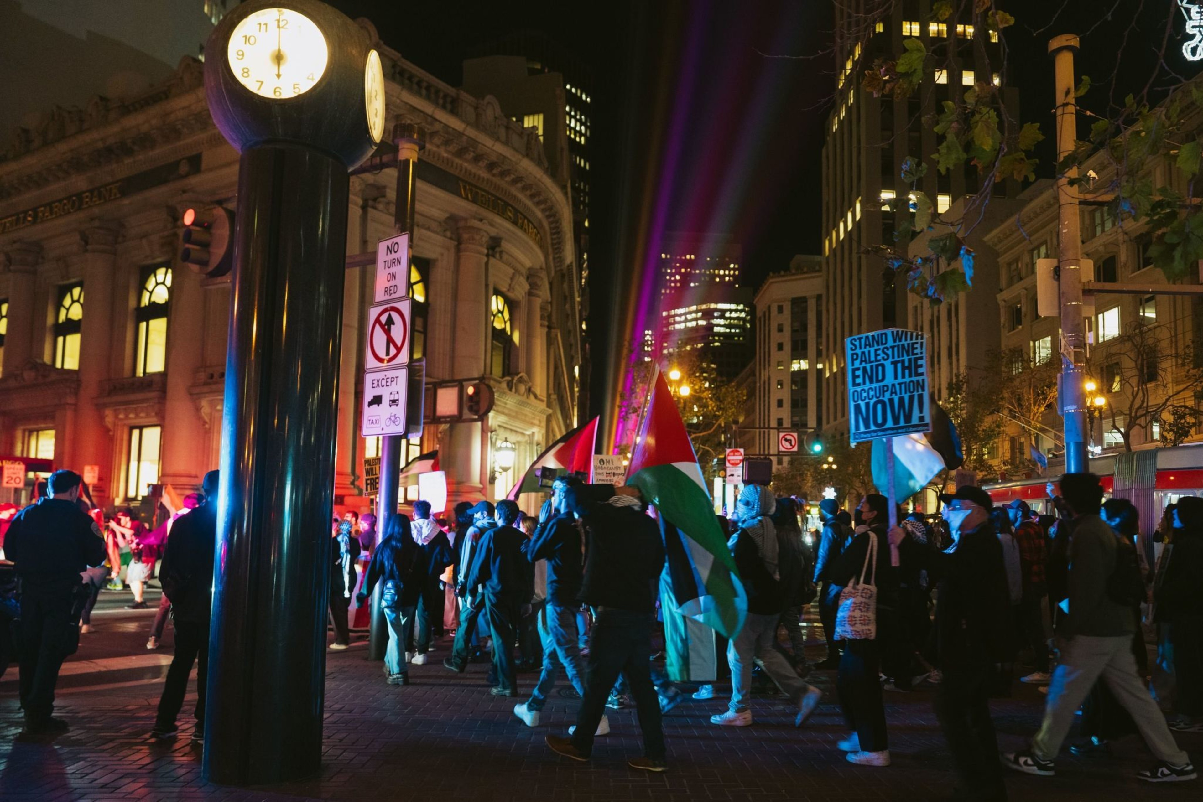 Protesters holding Palestinian flags march through a city street at night.