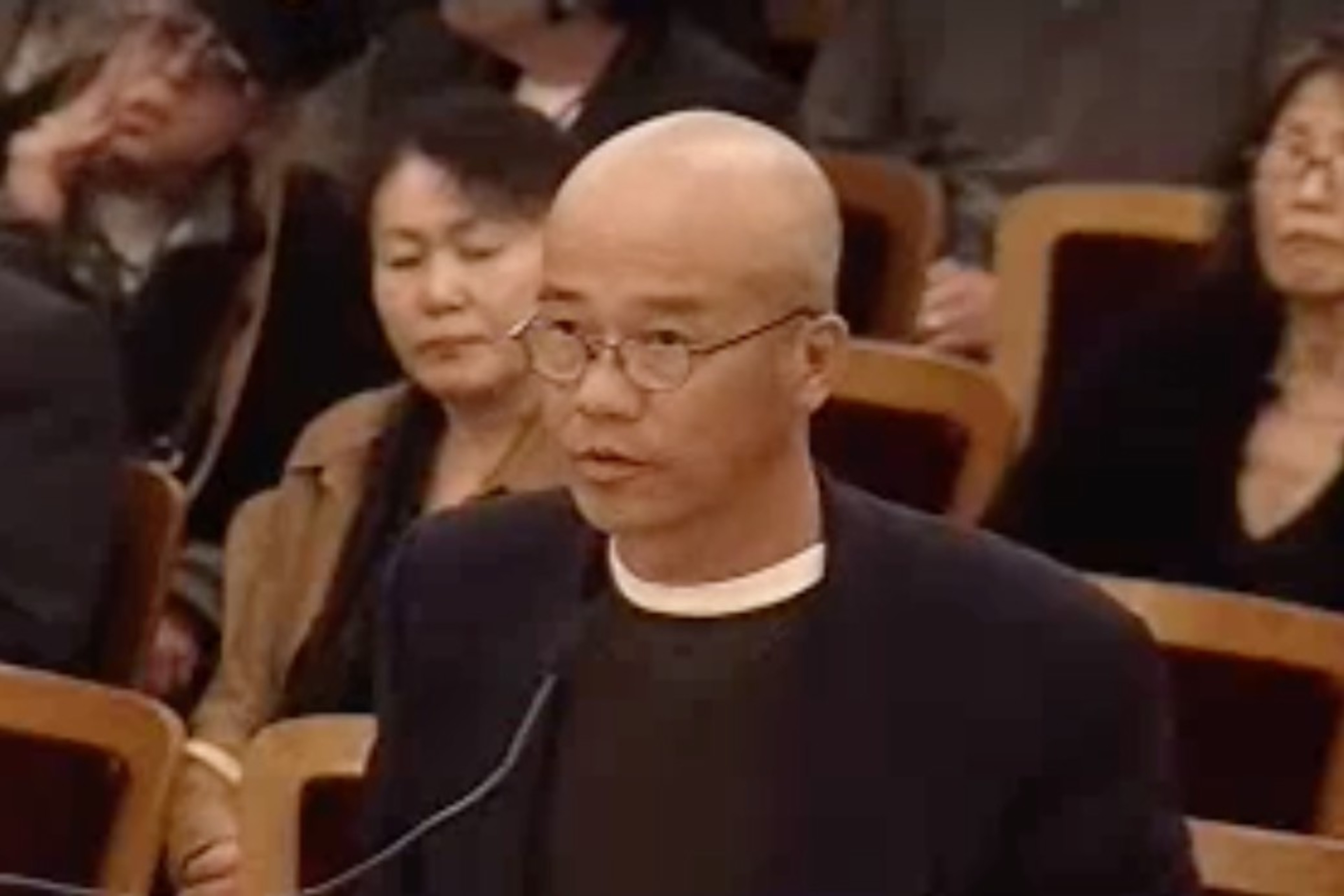 A bald man speaks to a commission.