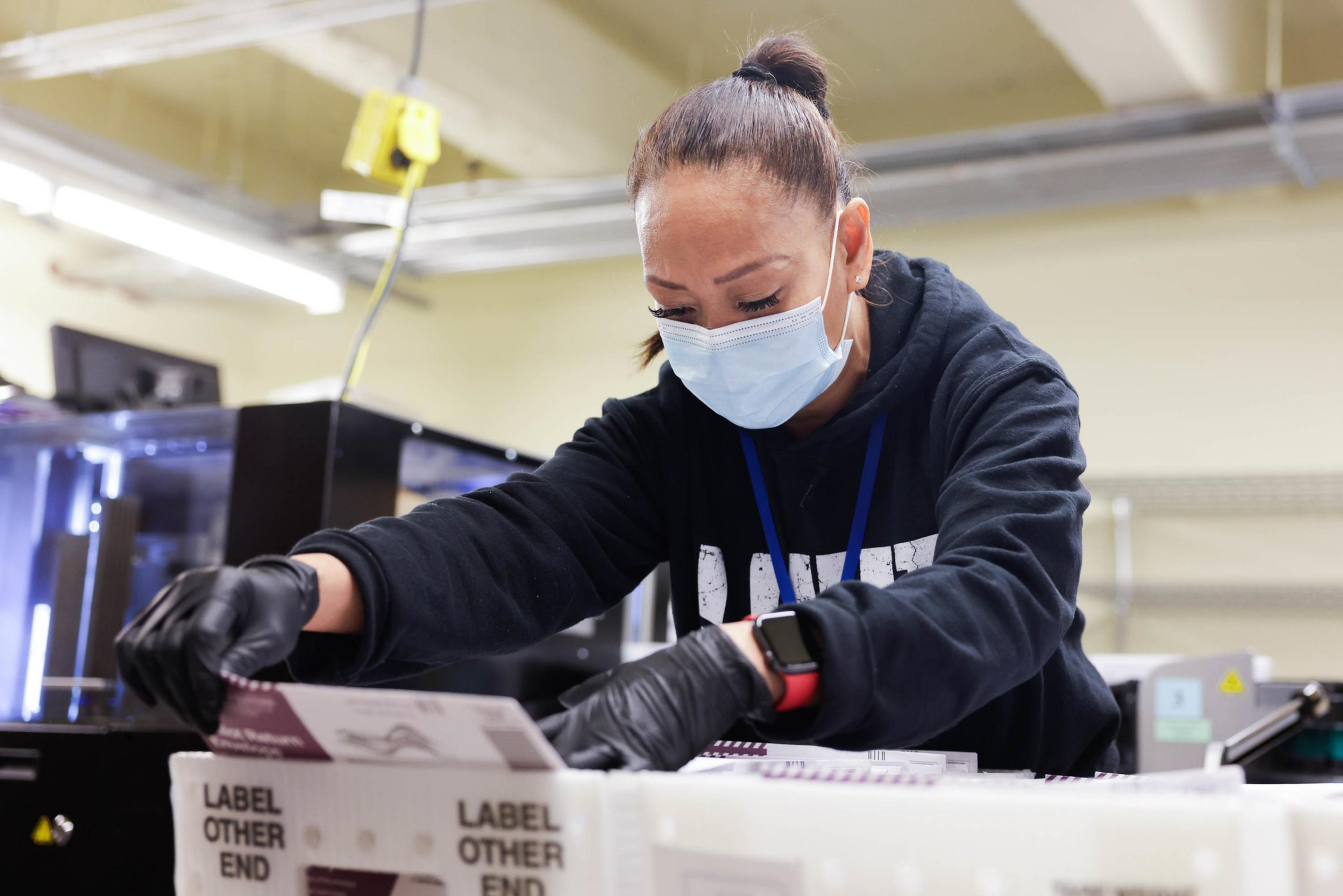 A woman wearing a mask and gloves works diligently with ballots at city hall.