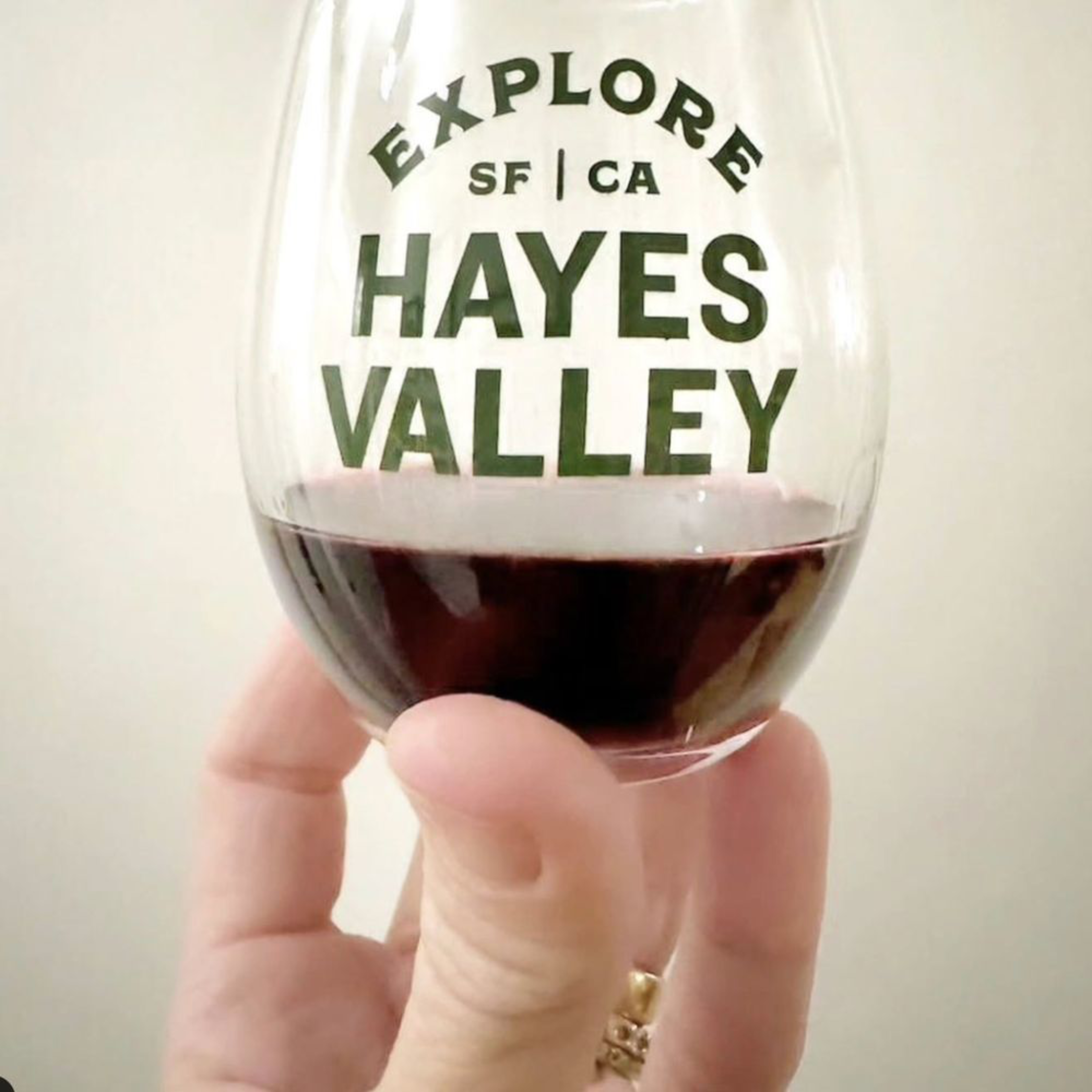 A hand holds a small glass of red wine with the words "EXPLORE SF | CA HAYES VALLEY" printed on it.