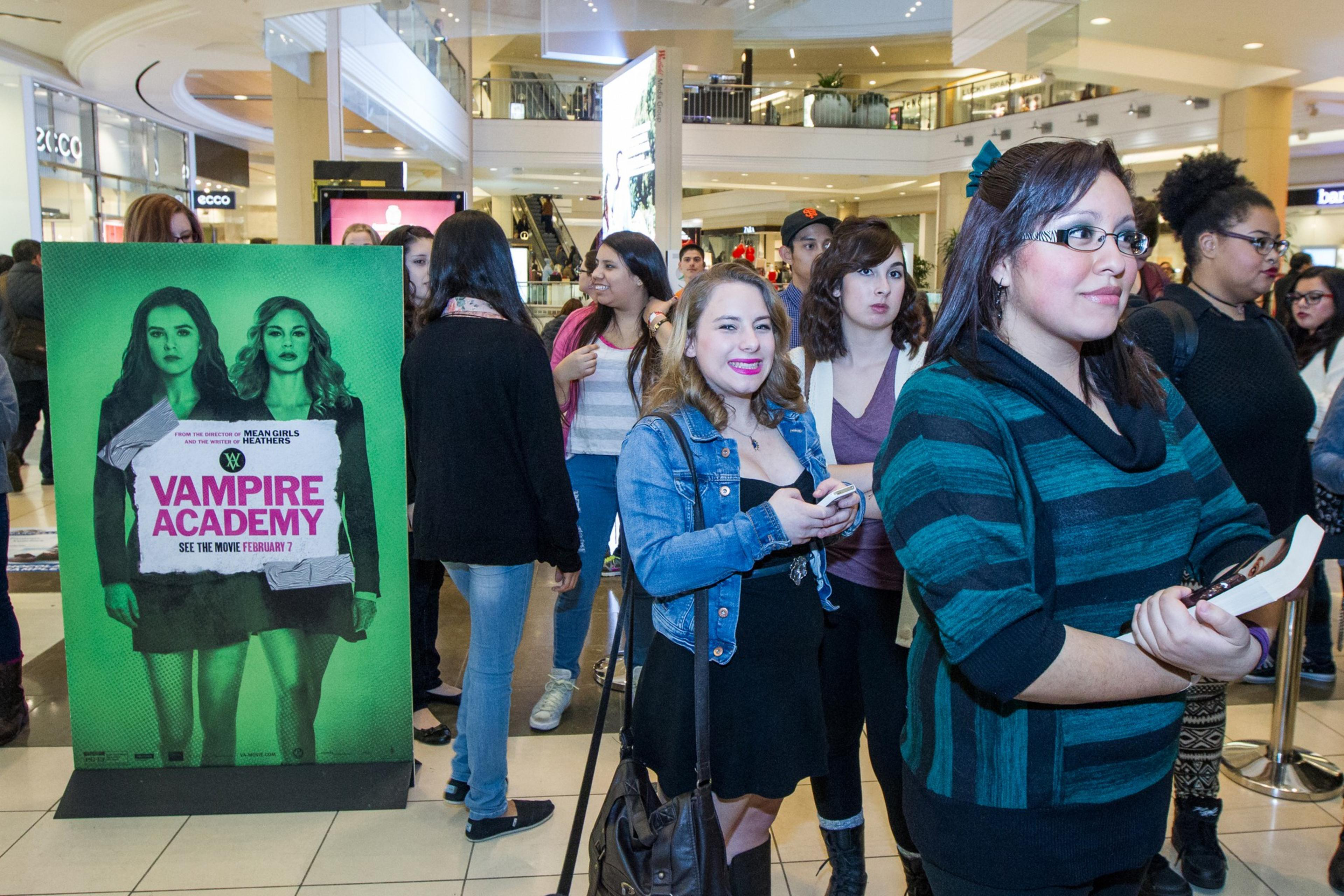 People wait in a mall beside a "Vampire Academy" movie sign.