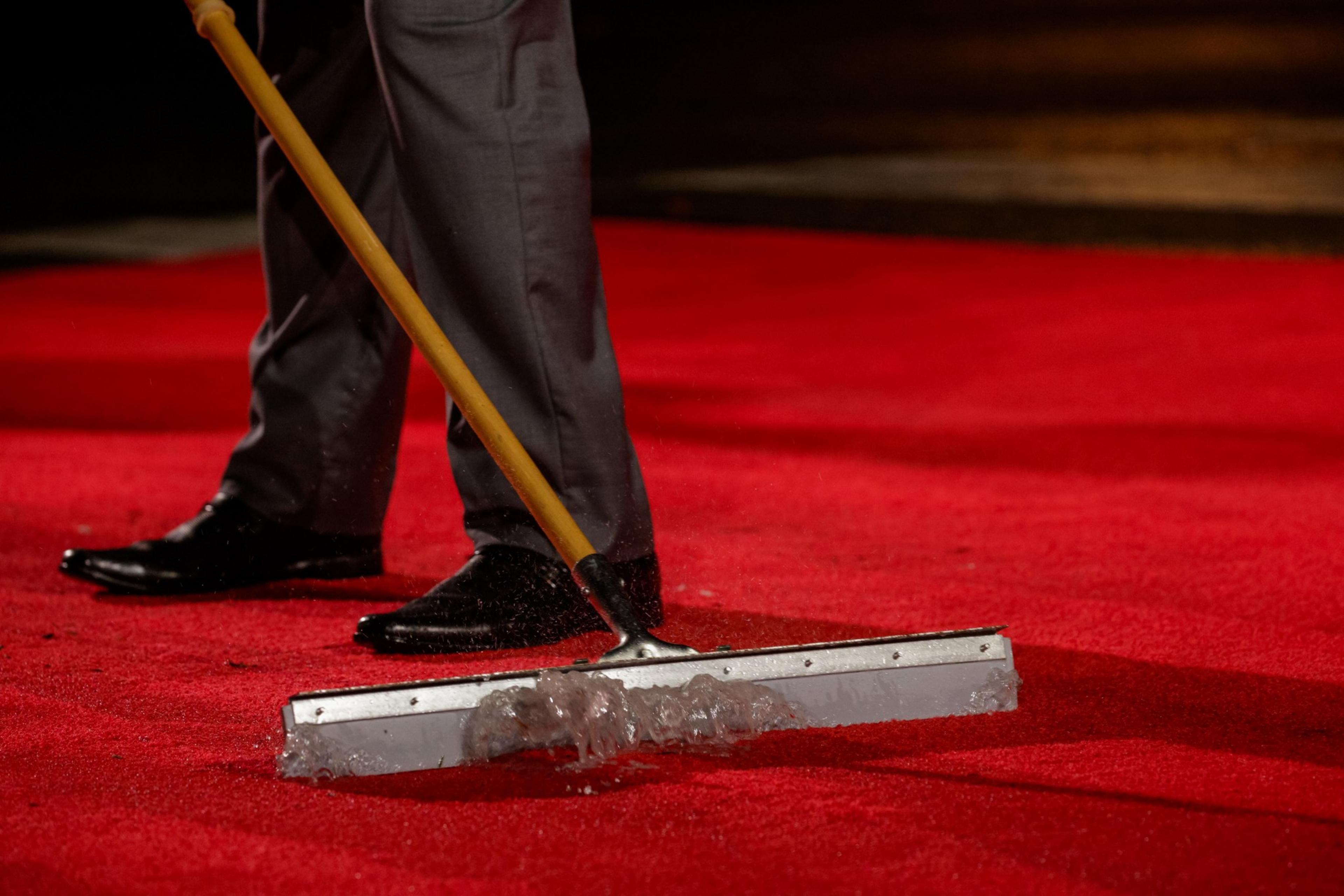 a State Department aide scrapes pools of water off a red carpet at the Legion of Honor Museum, where world leaders gathered during APEC. 