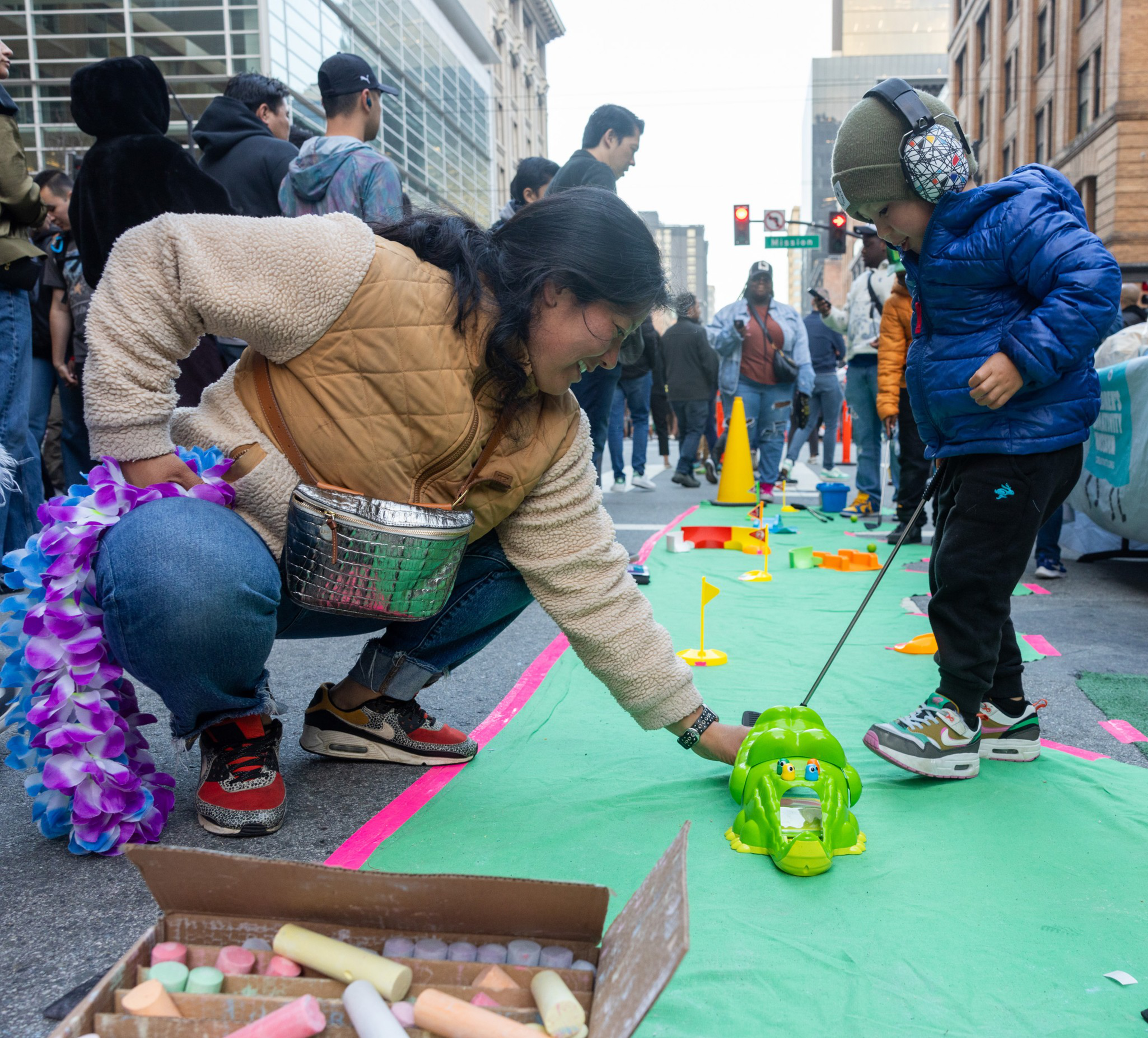 A woman helps a child play mini golf. 