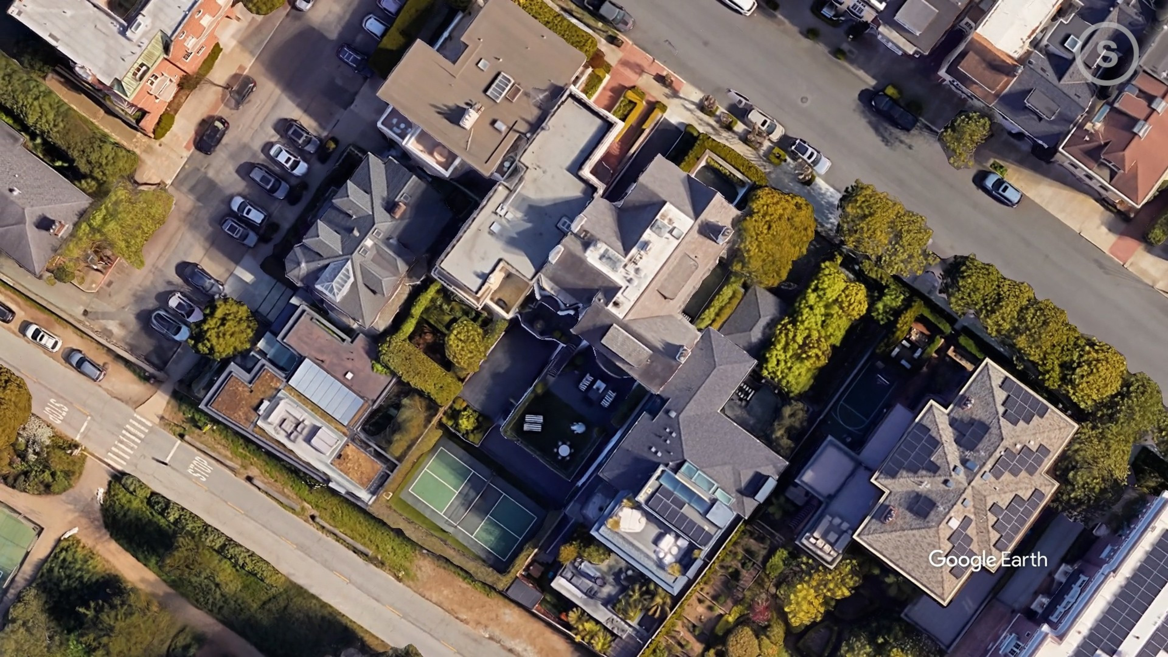 Aerial view of a neighborhood with houses, trees, cars and a tennis court.