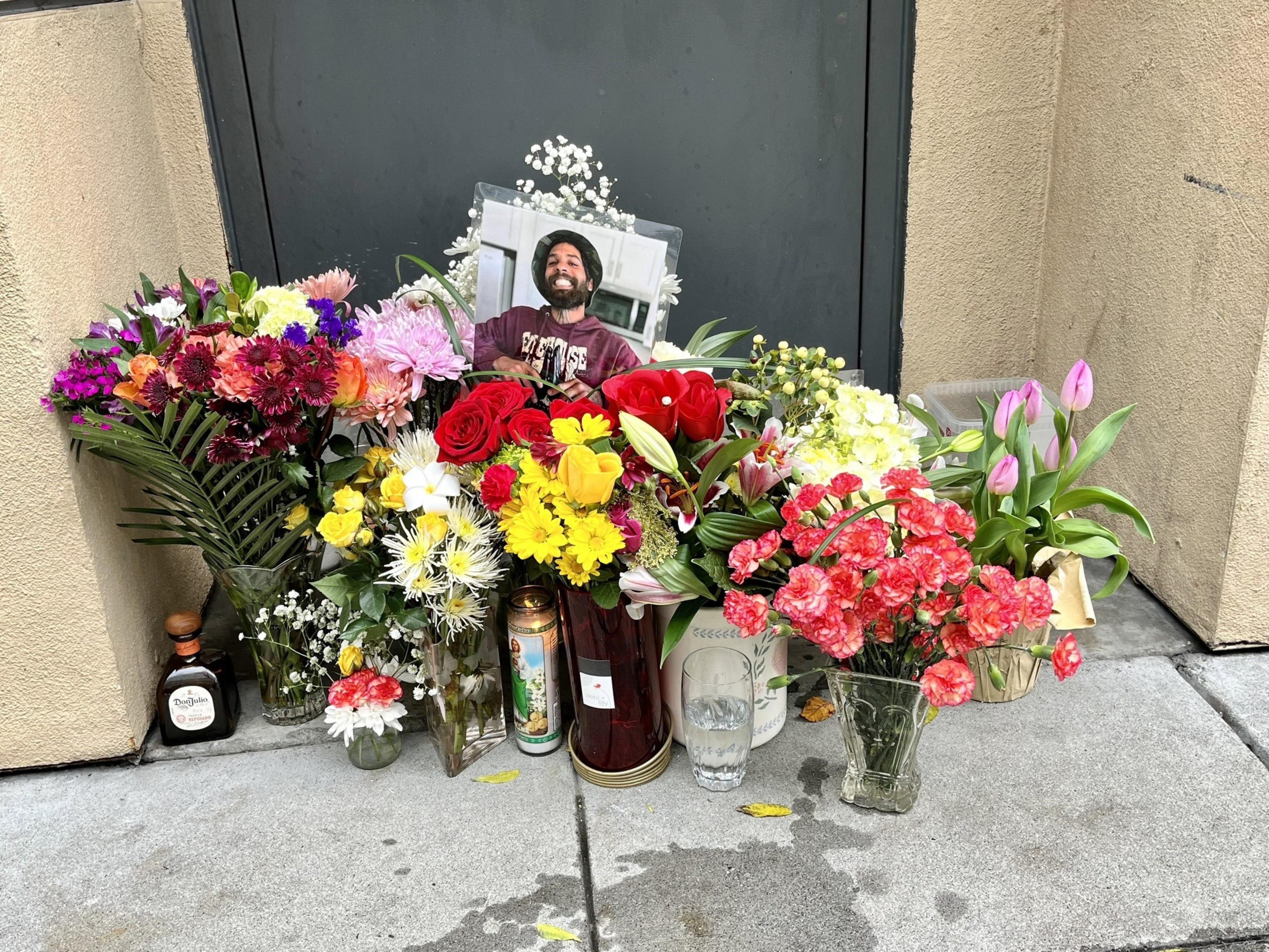 A memorial with flowers and a framed photo against a dark doorway.