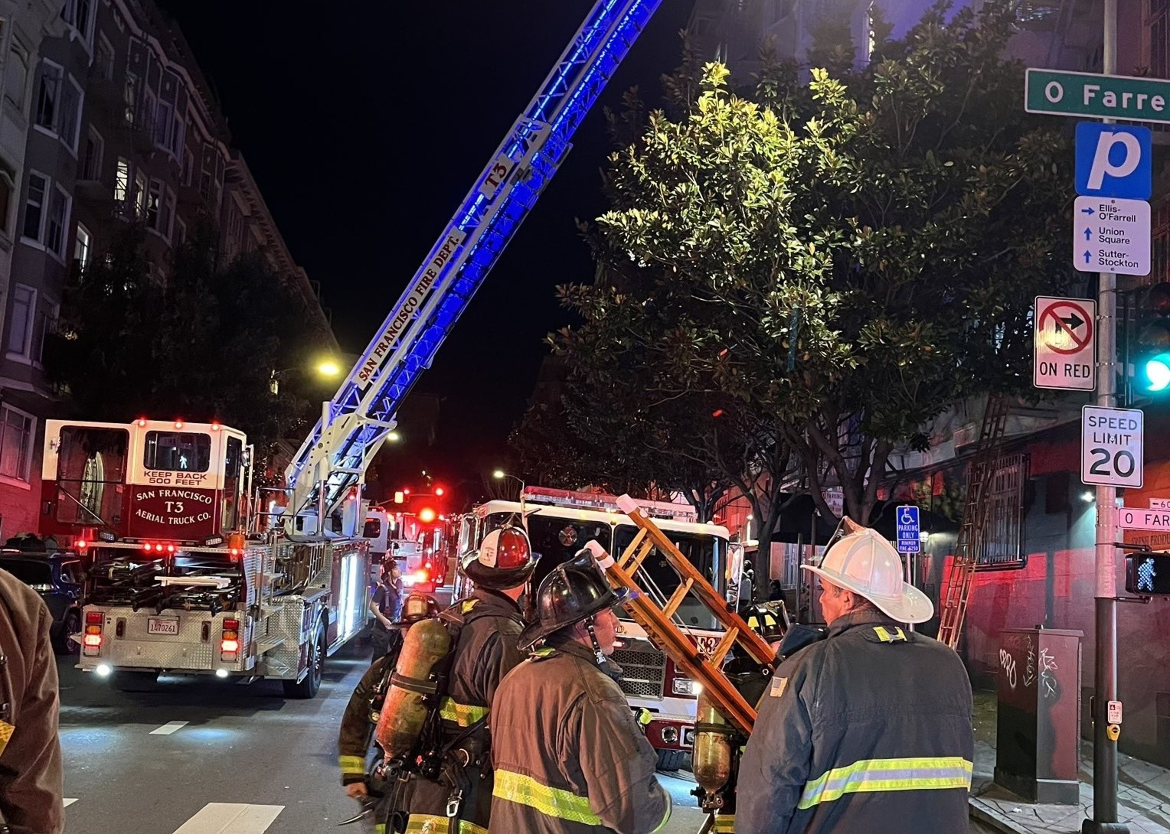 A fire engine and fire truck with a ladder with firefighters stand outside an apartment building at nighttime.