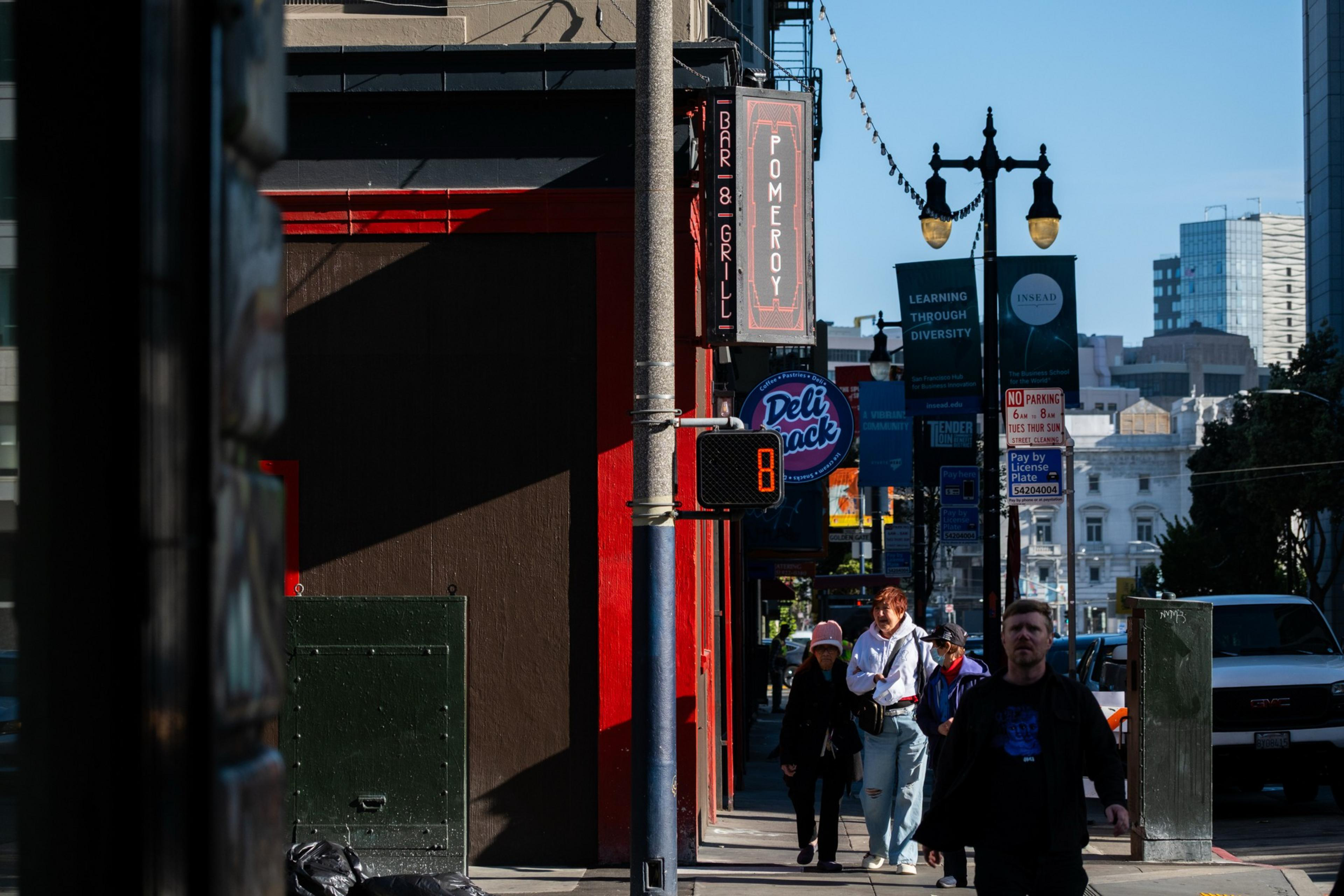 A city street scene shows pedestrians walking under a bar sign, streetlights, and various shop signs, with an 8-second countdown on a crosswalk signal.