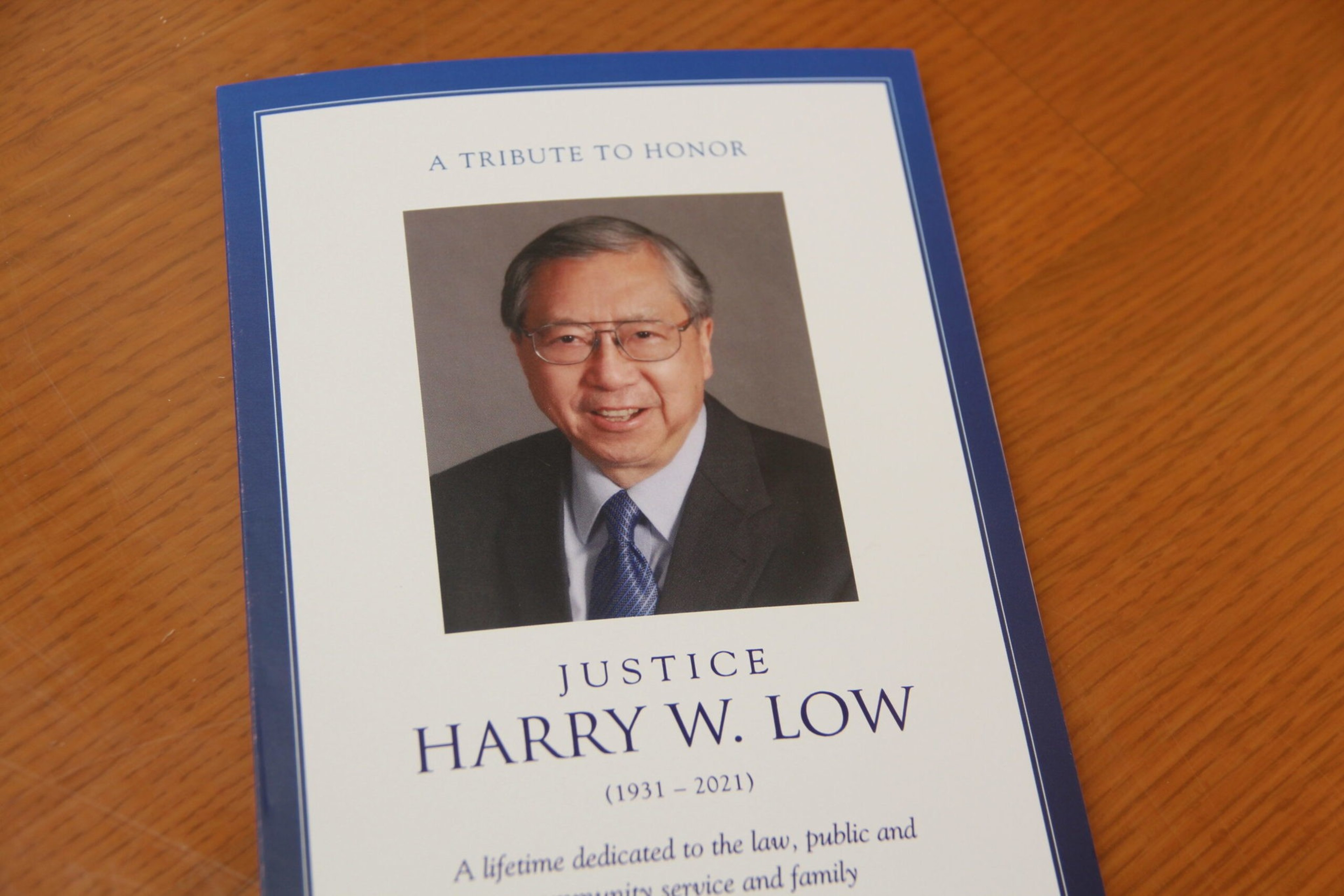 A tribute card honors Justice Harry W. Low (1931-2021) with his photo, mentioning his dedication to law, public and community service, and family.