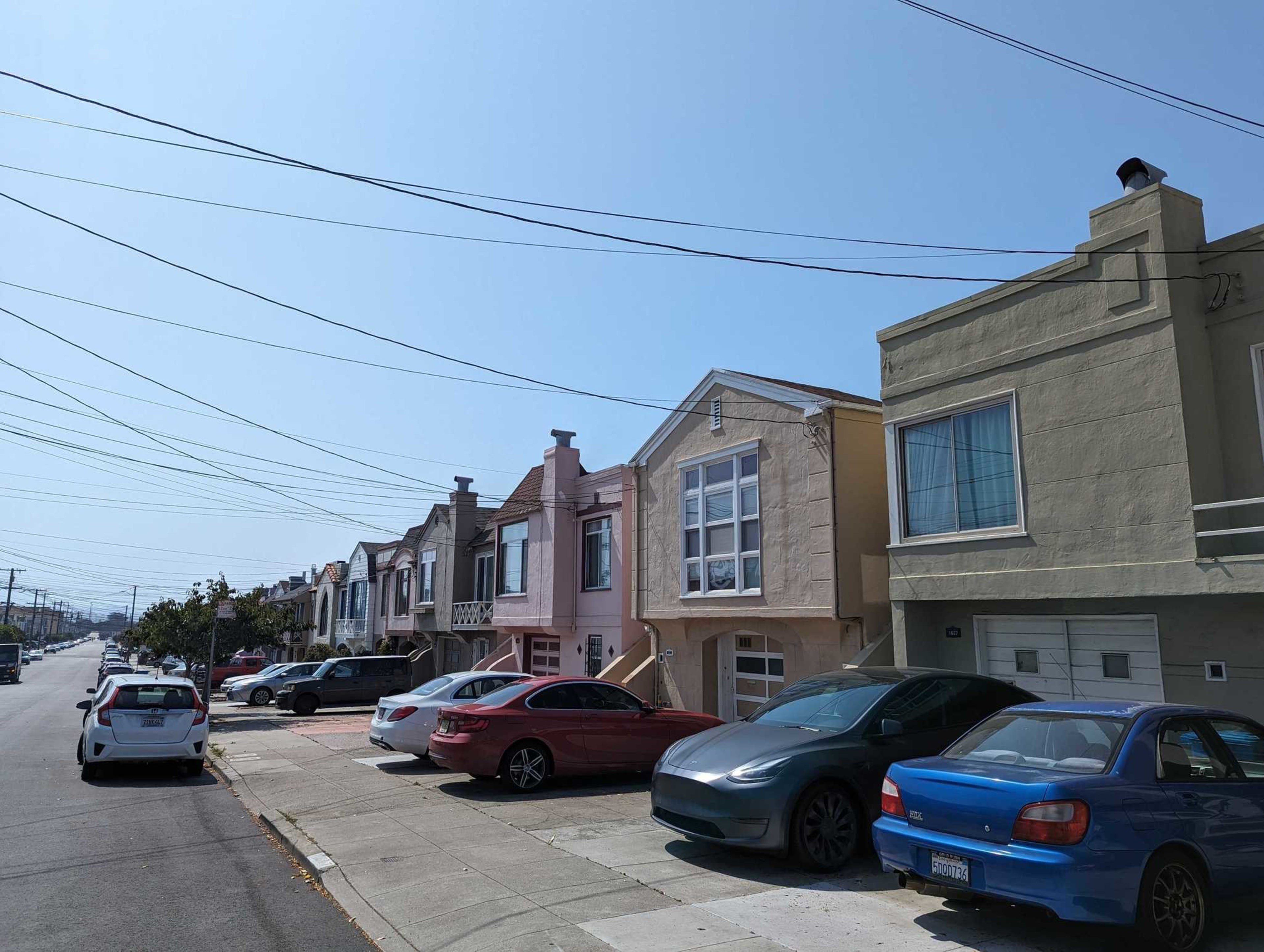 Row of colorful houses with parked cars under a clear blue sky, with overhanging power lines.