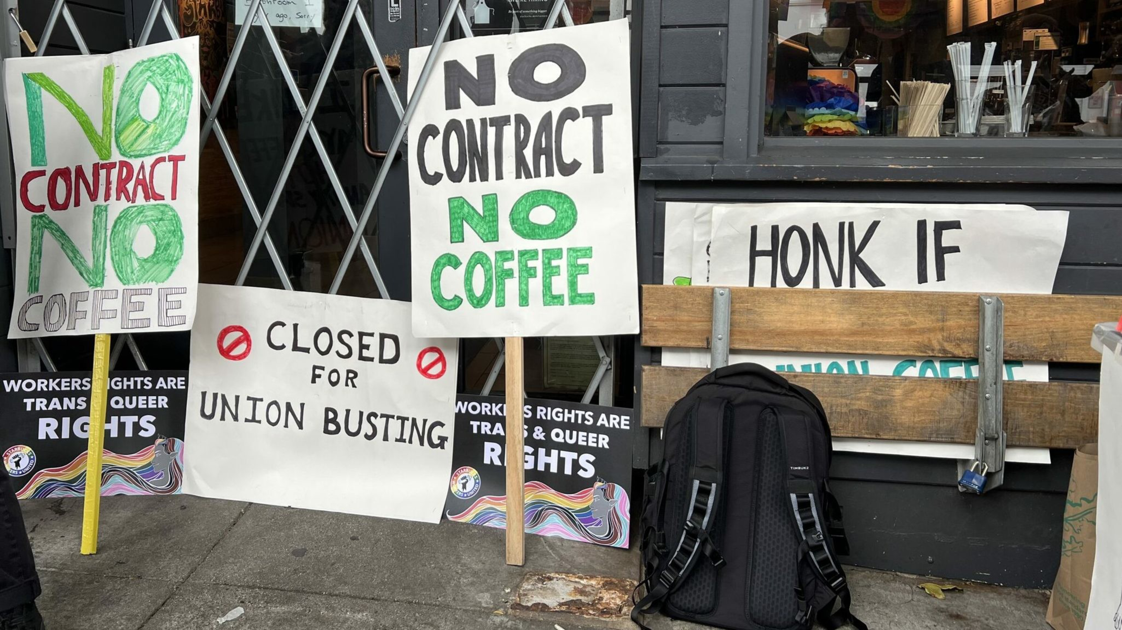 Signs reading "No Contract No Coffee," "Closed for Union Busting," and "Workers Rights Are Trans & Queer Rights" are displayed in front of a closed cafe.