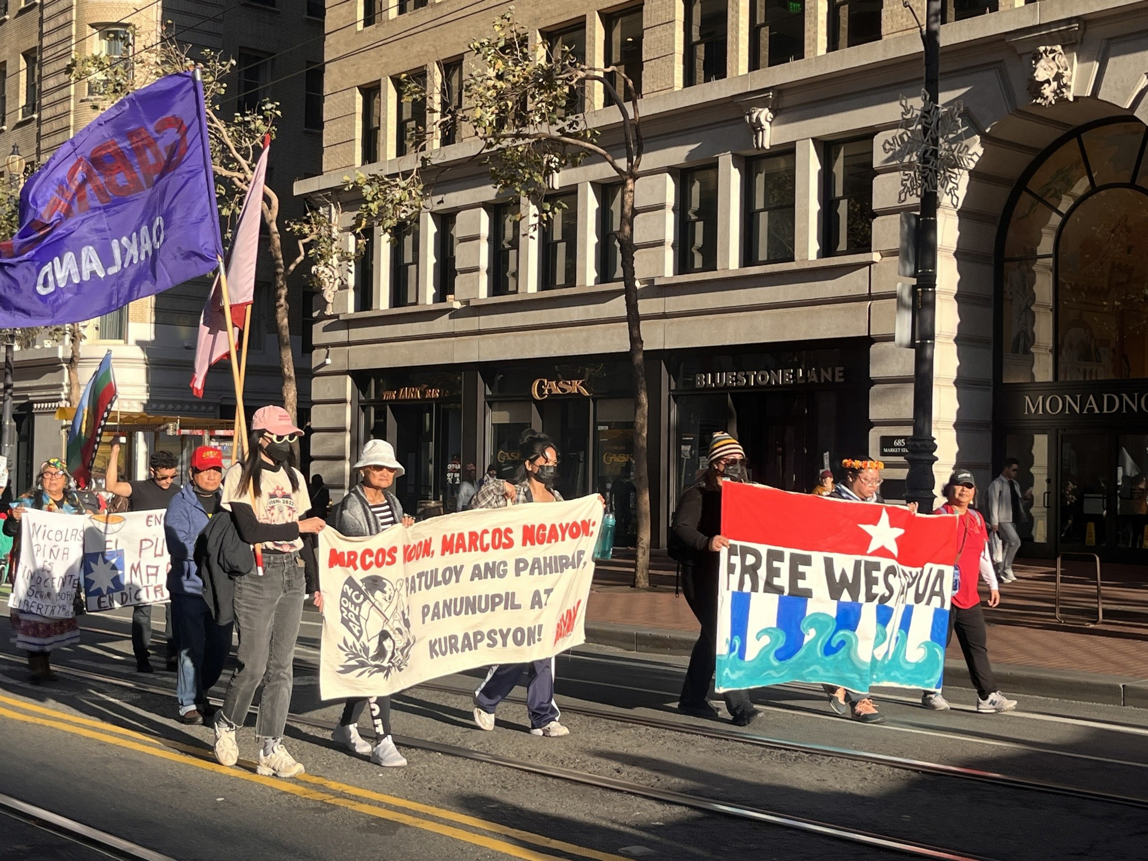 A group of people carrying flags banners against the Philippine government and other matters march along a street.
