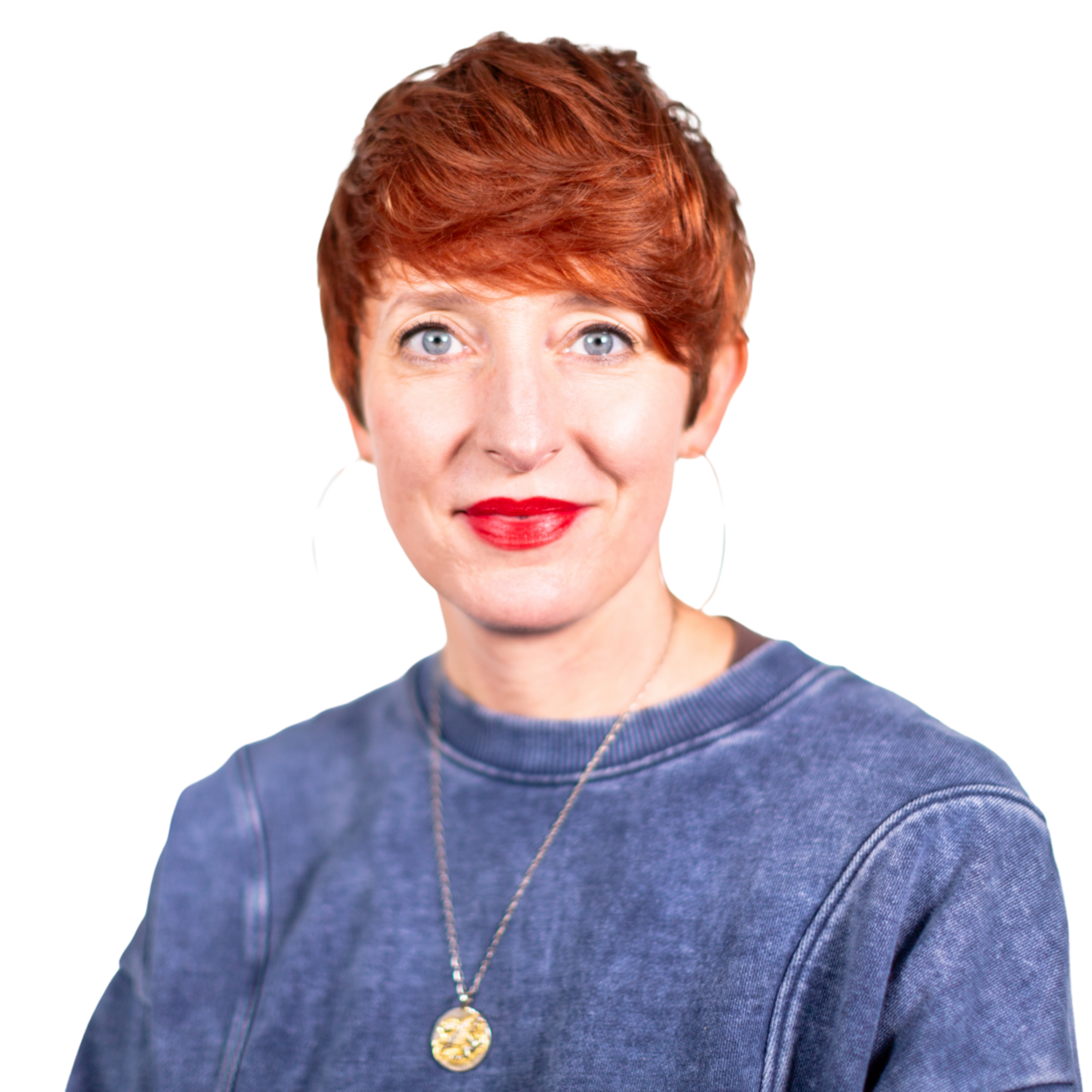 A woman with short red hair and bright red lipstick wears large hoop earrings, a blue sweatshirt, and a gold pendant necklace, smiling slightly.