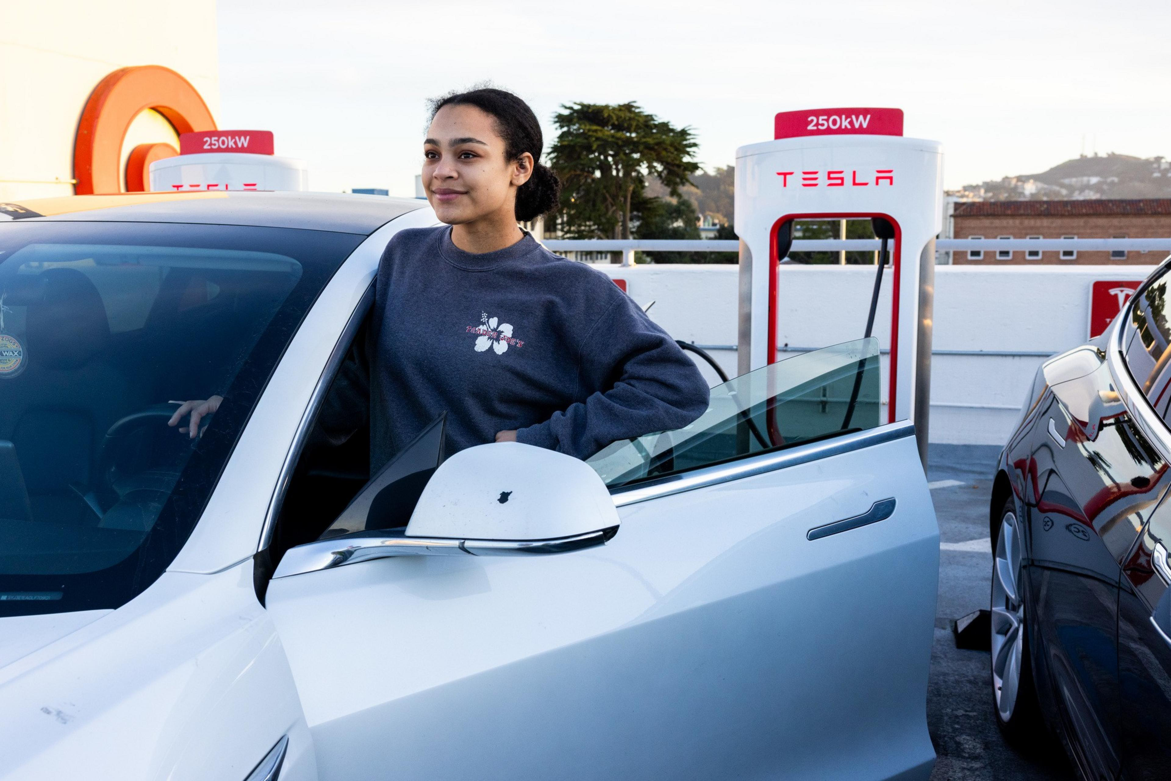 A woman standing next to a Tesla charging station