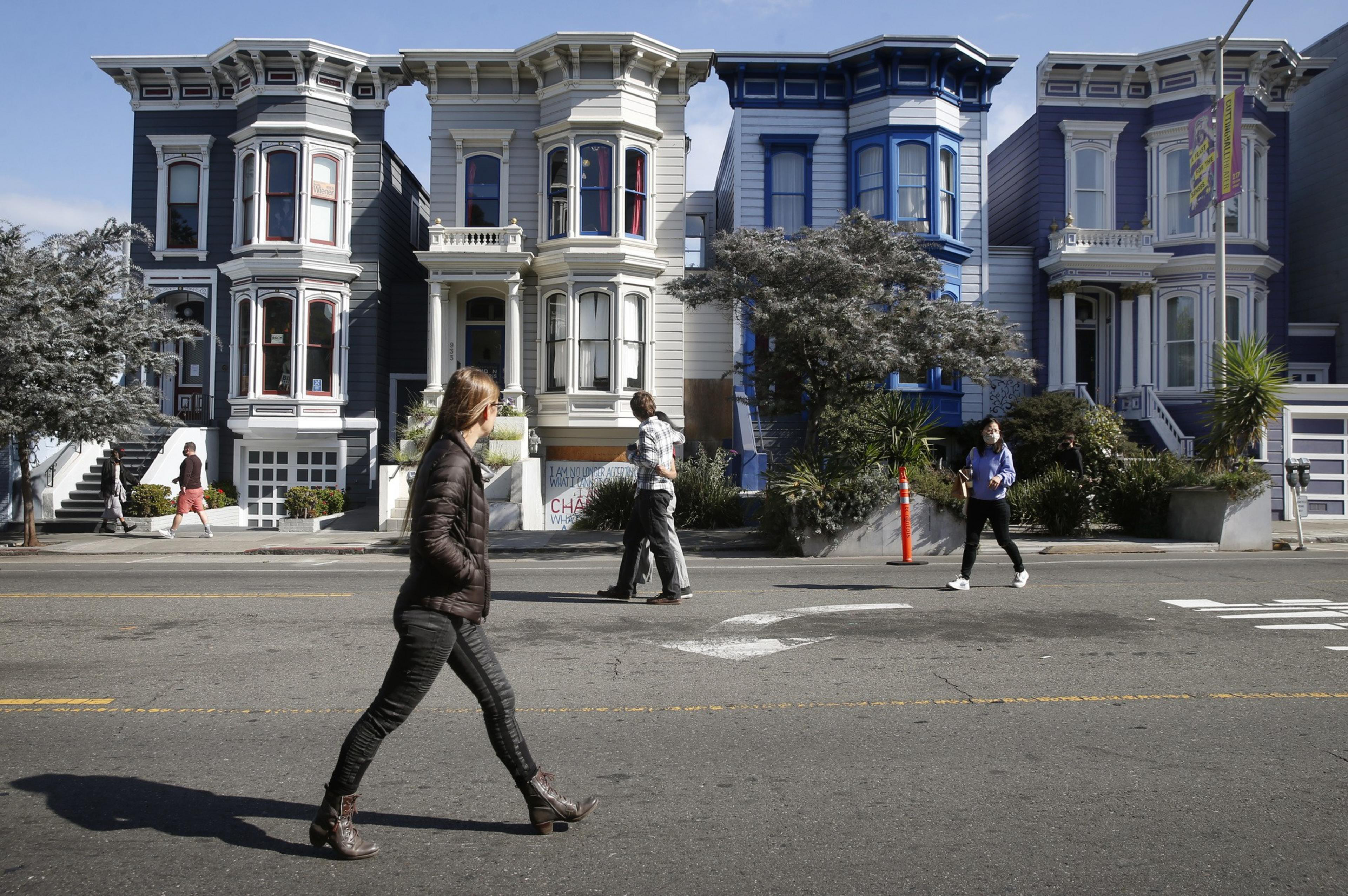 A woman walks in the middle of an otherwise open street, with Victorian homes in the background.