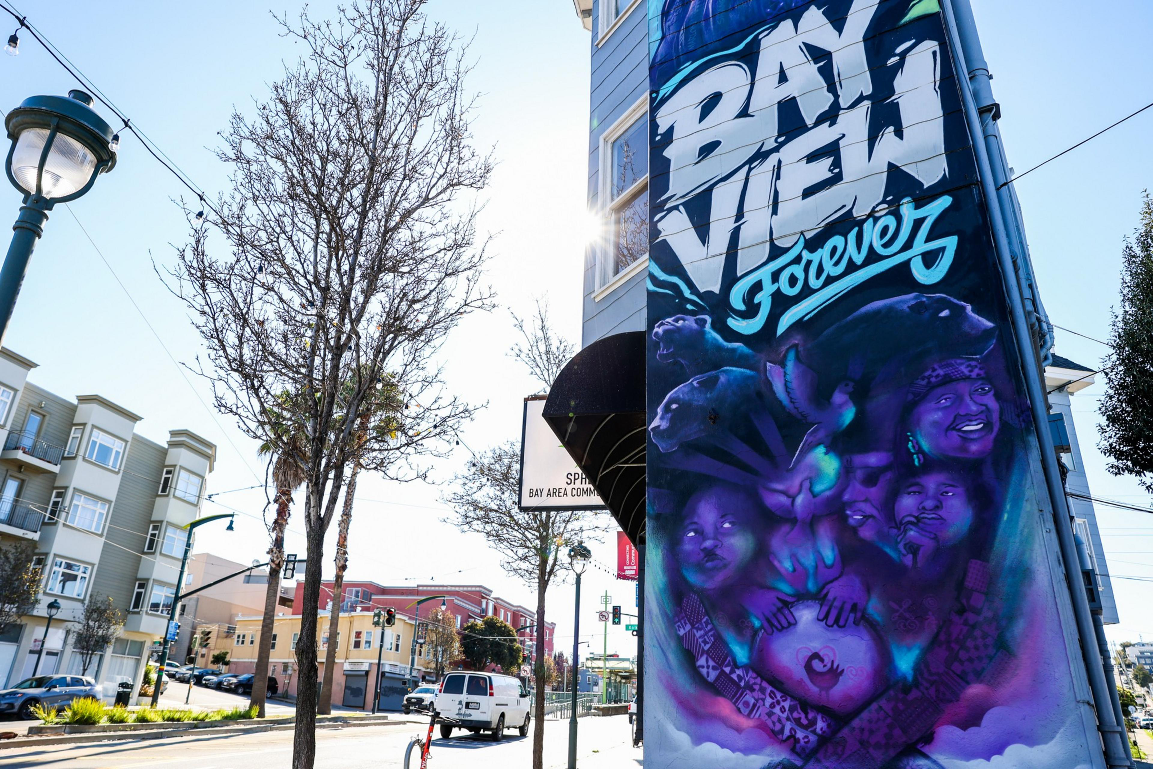 A colorful mural on a building reads "BAY VIEW Forever" with portraits of smiling people and a bird, set against a bright urban street scene.