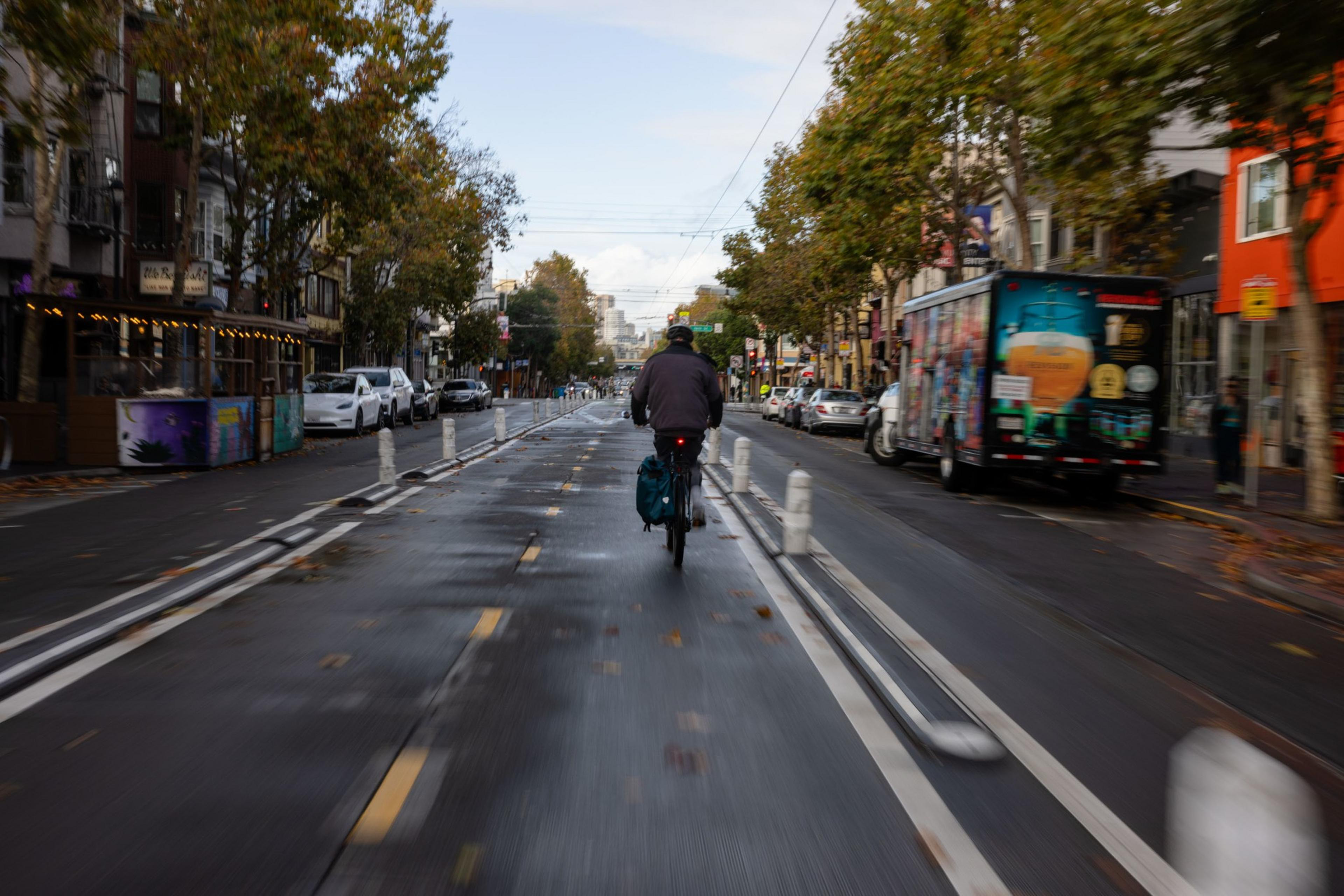A cyclist bikes away on a wet bike lane during the day.
