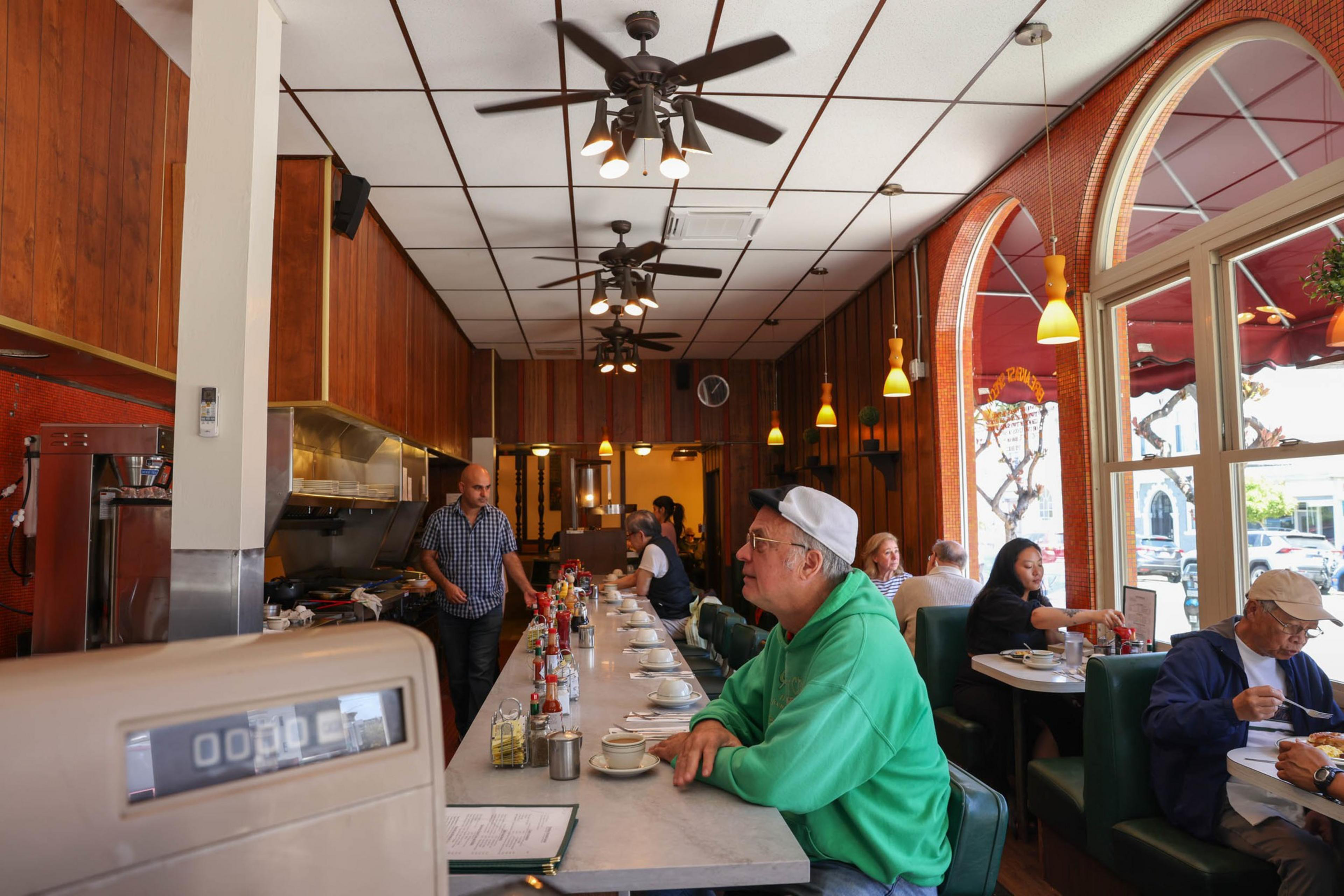 A diner with wooden walls and ceiling fans, counter seating, and window tables. People are dining, and a staff member is working behind the counter.