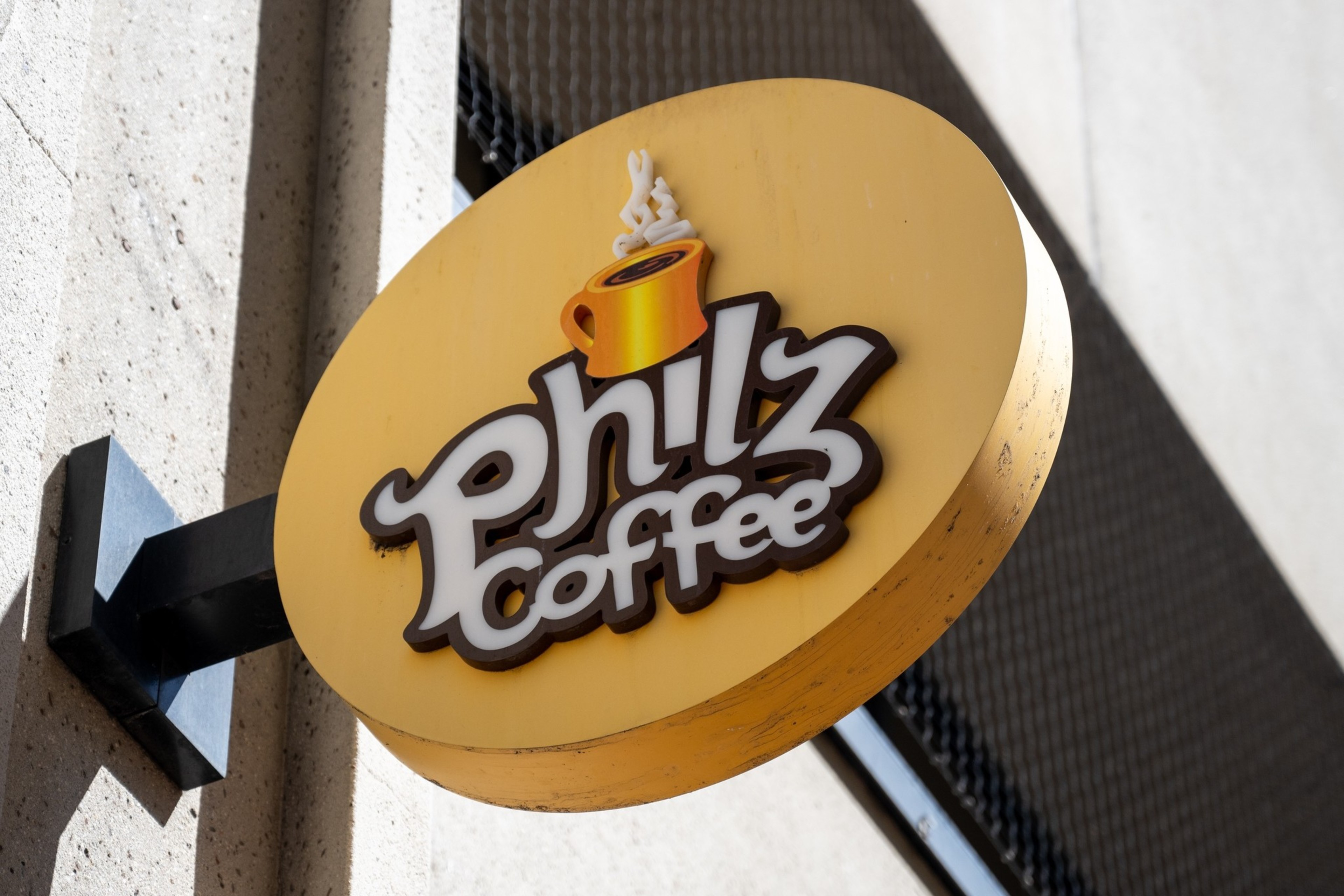 A round yellow sign attached to a wall displays the words "Philz Coffee" with a steaming orange coffee cup above the text.