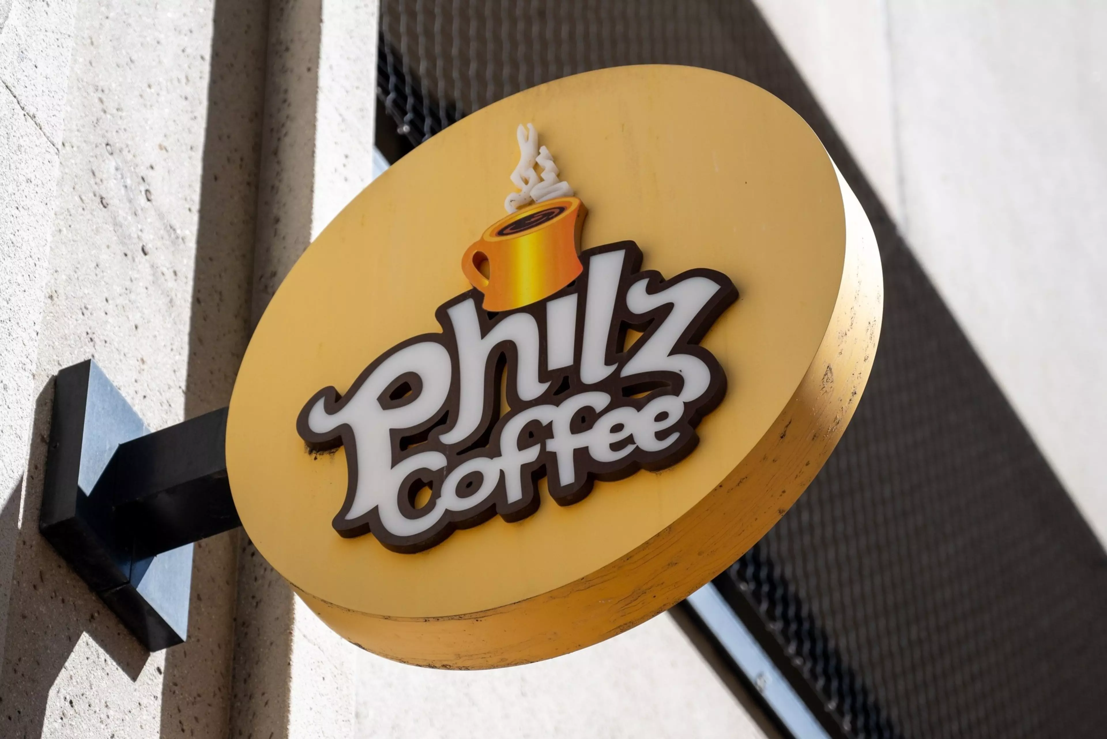 A round yellow sign attached to a wall displays the words "Philz Coffee" with a steaming orange coffee cup above the text.