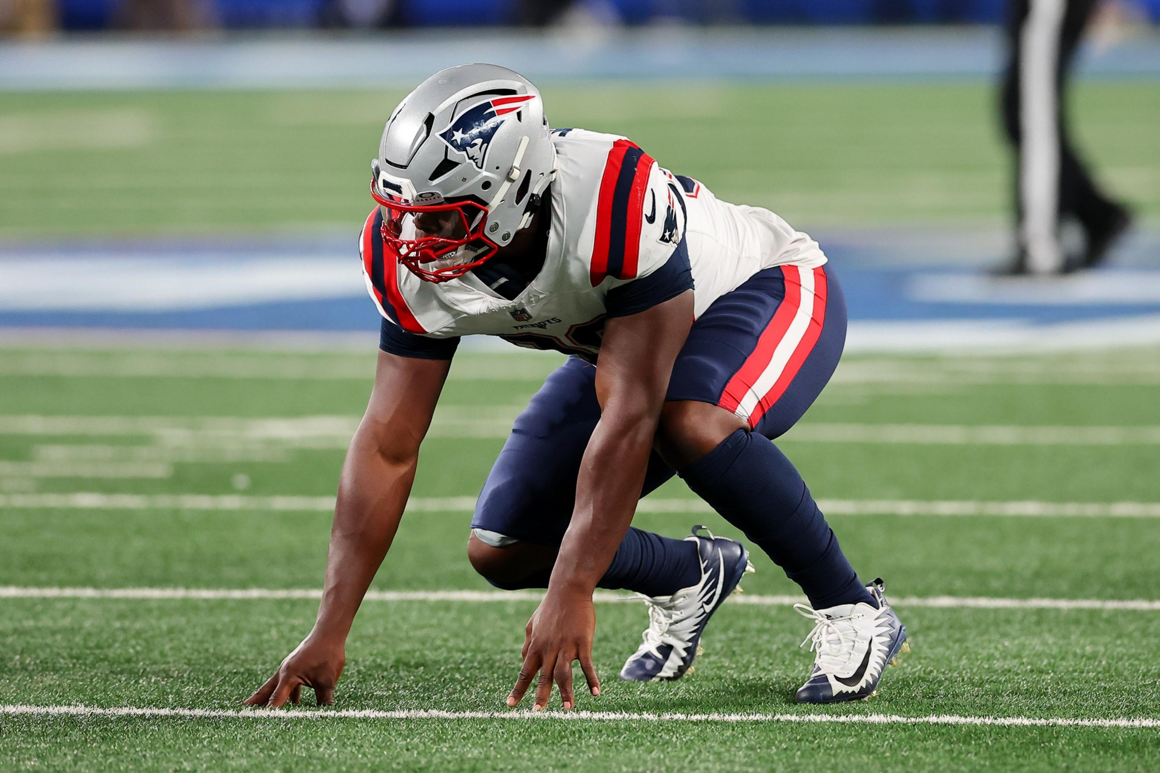 A football player in a New England Patriots uniform is crouched low on the field, ready to start a play.