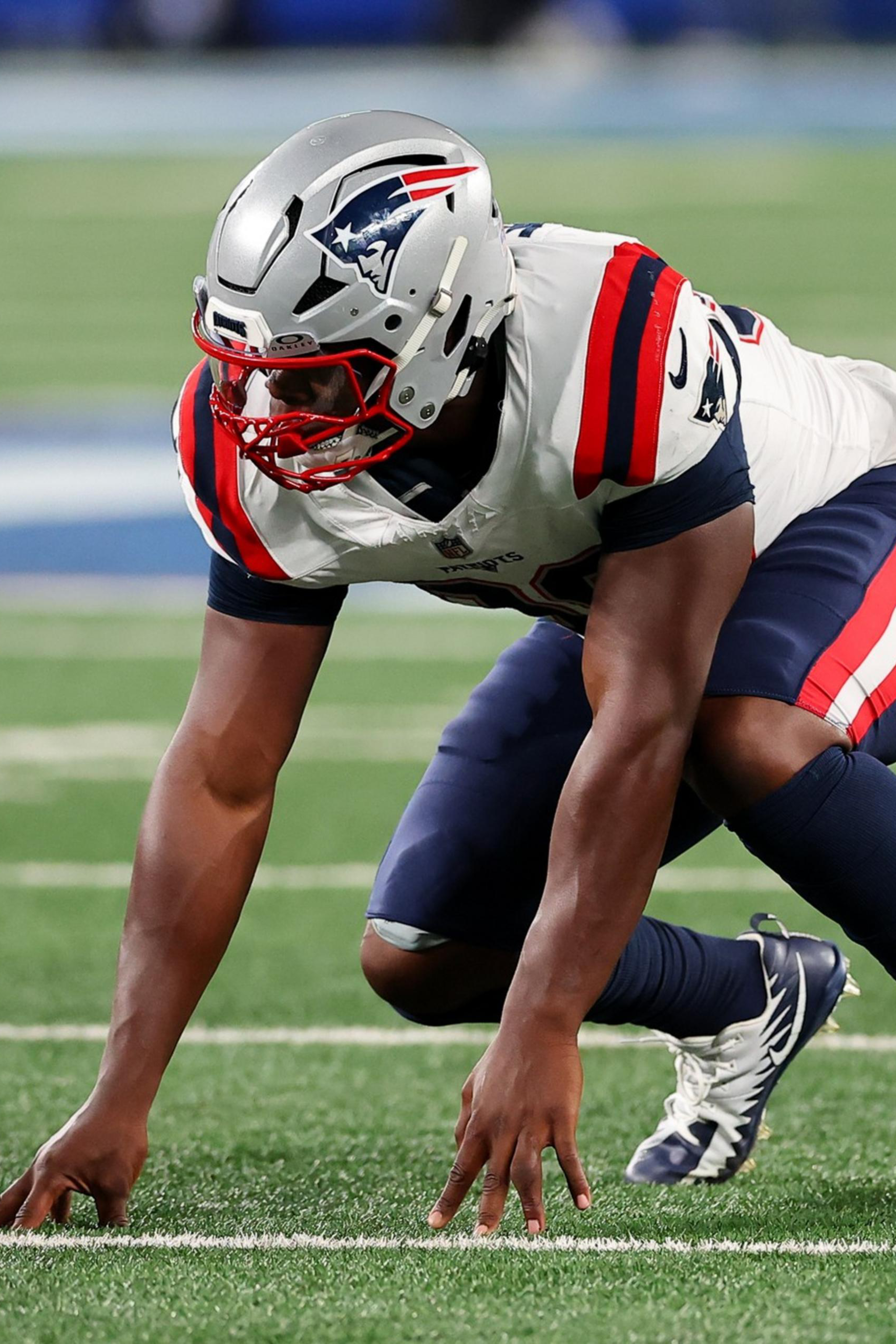 A football player in a New England Patriots uniform is crouched low on the field, ready to start a play.